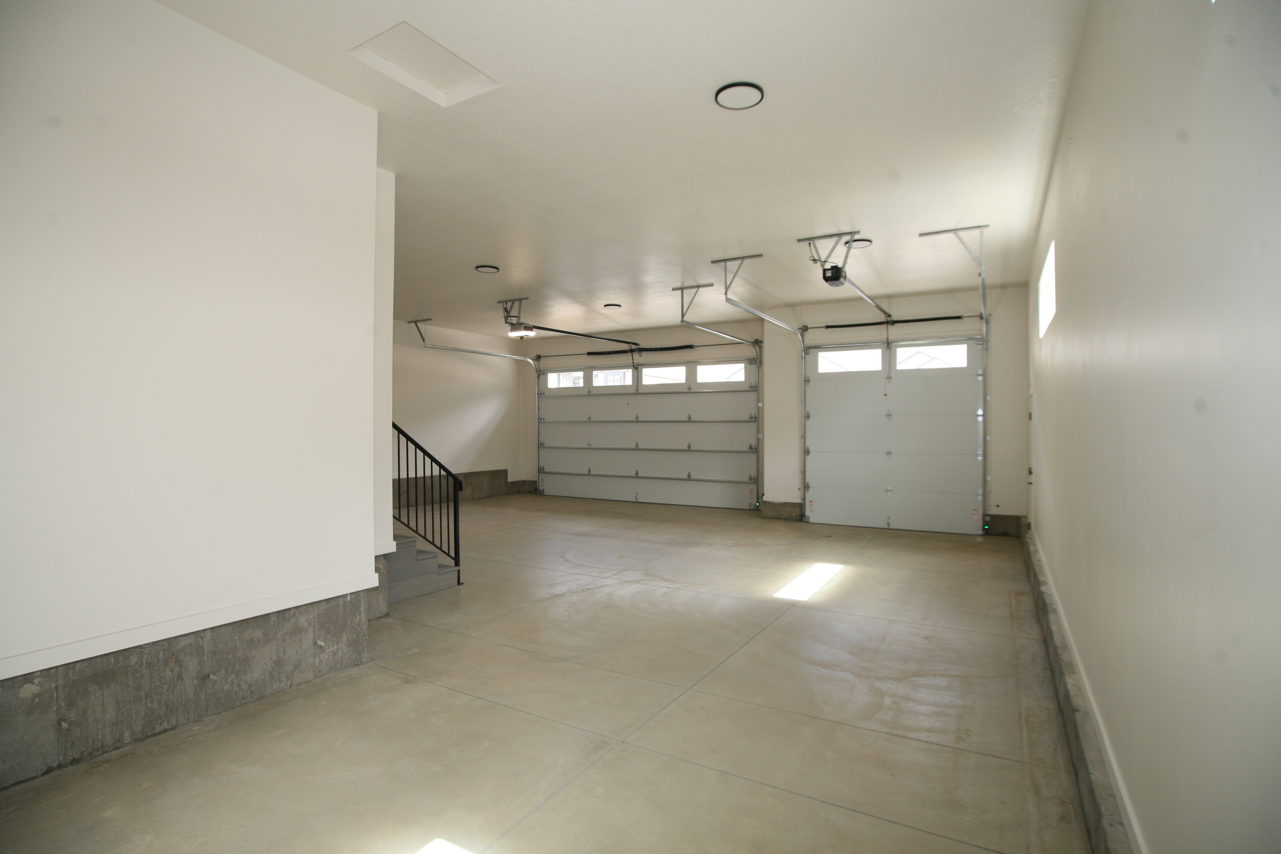 Spacious three-car garage featuring a concrete floor, white walls, and two overhead garage doors with frosted window inserts