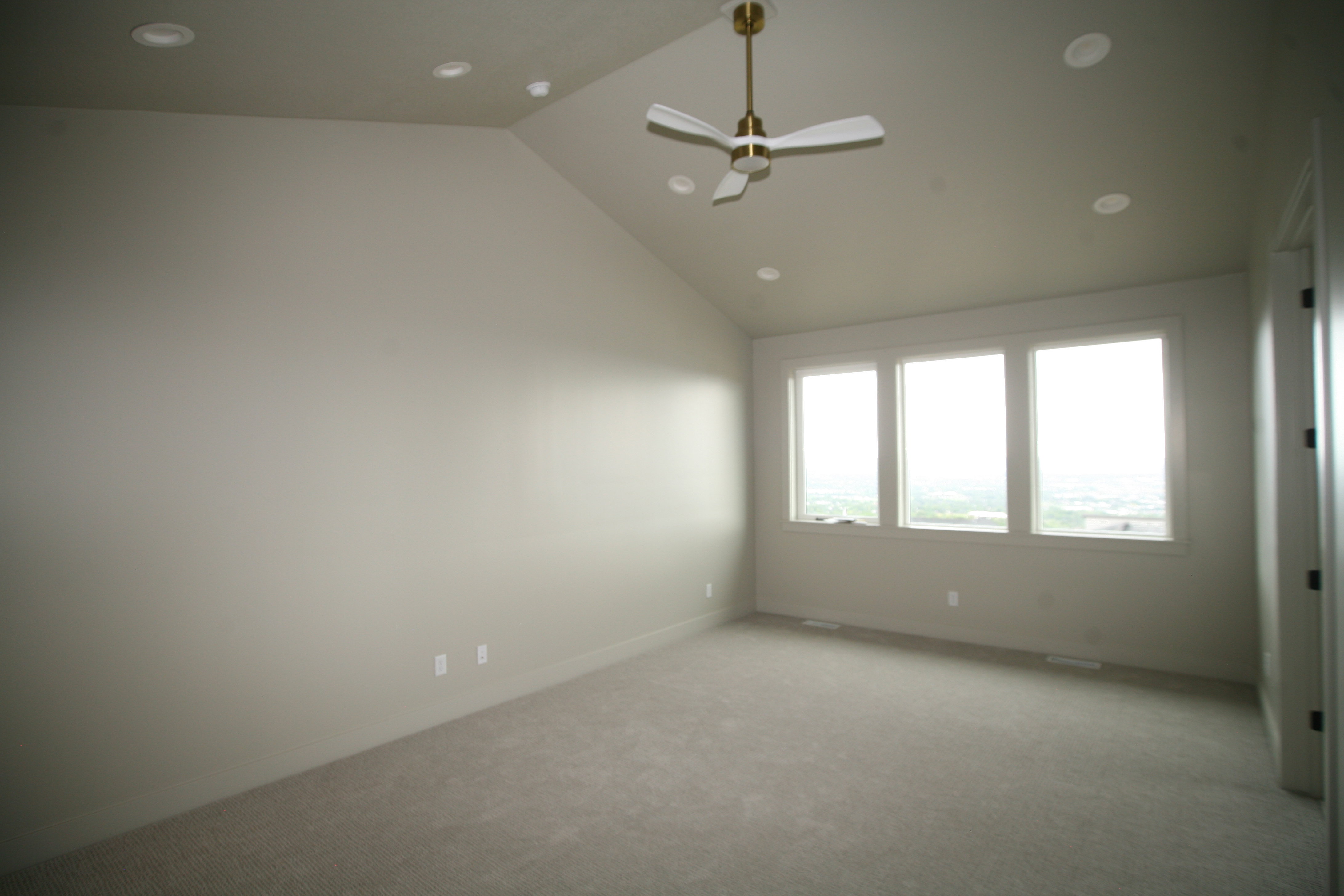 Spacious room featuring vaulted ceilings, a brass-finished ceiling fan, recessed lighting, and a triple window assembly