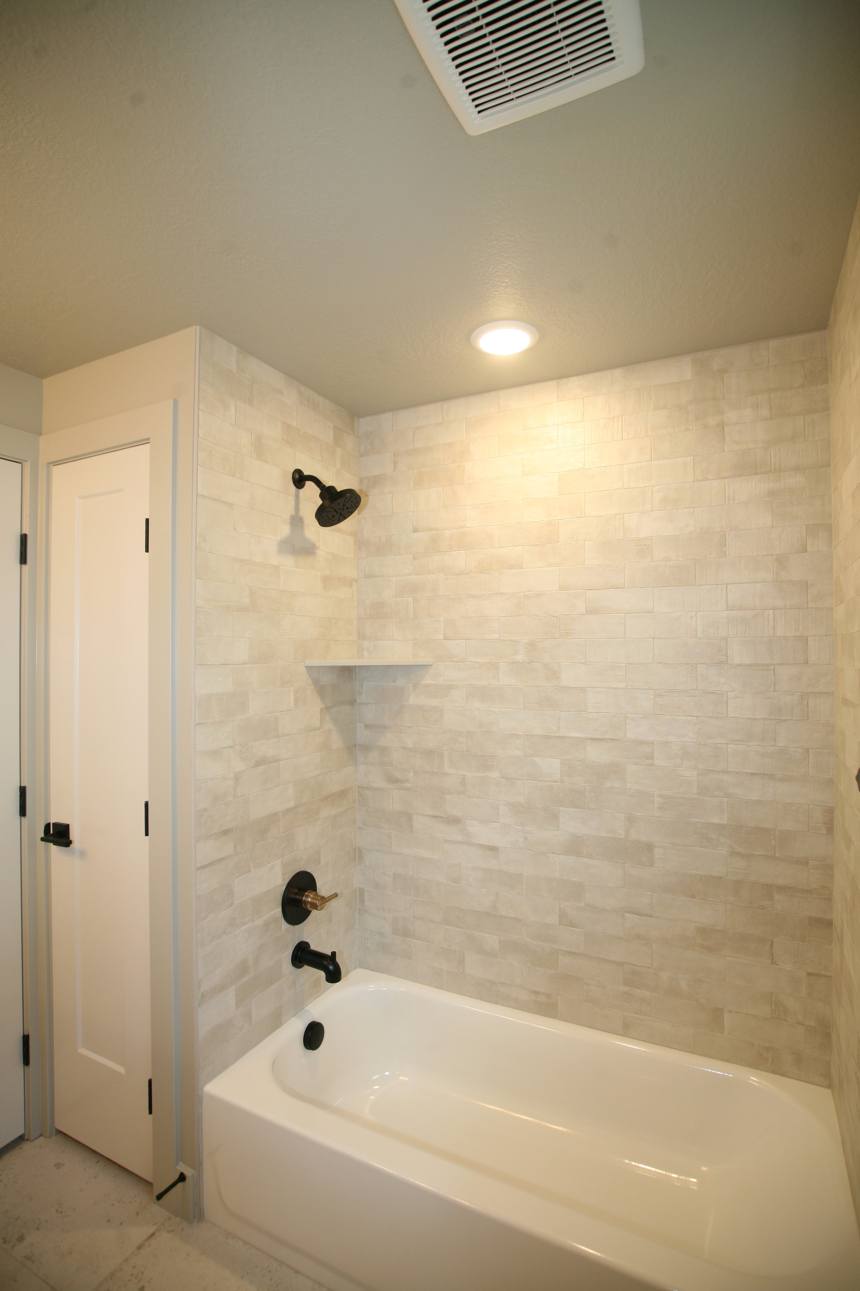 White bathtub with matte black fixtures and a stacked stone-look tile surround