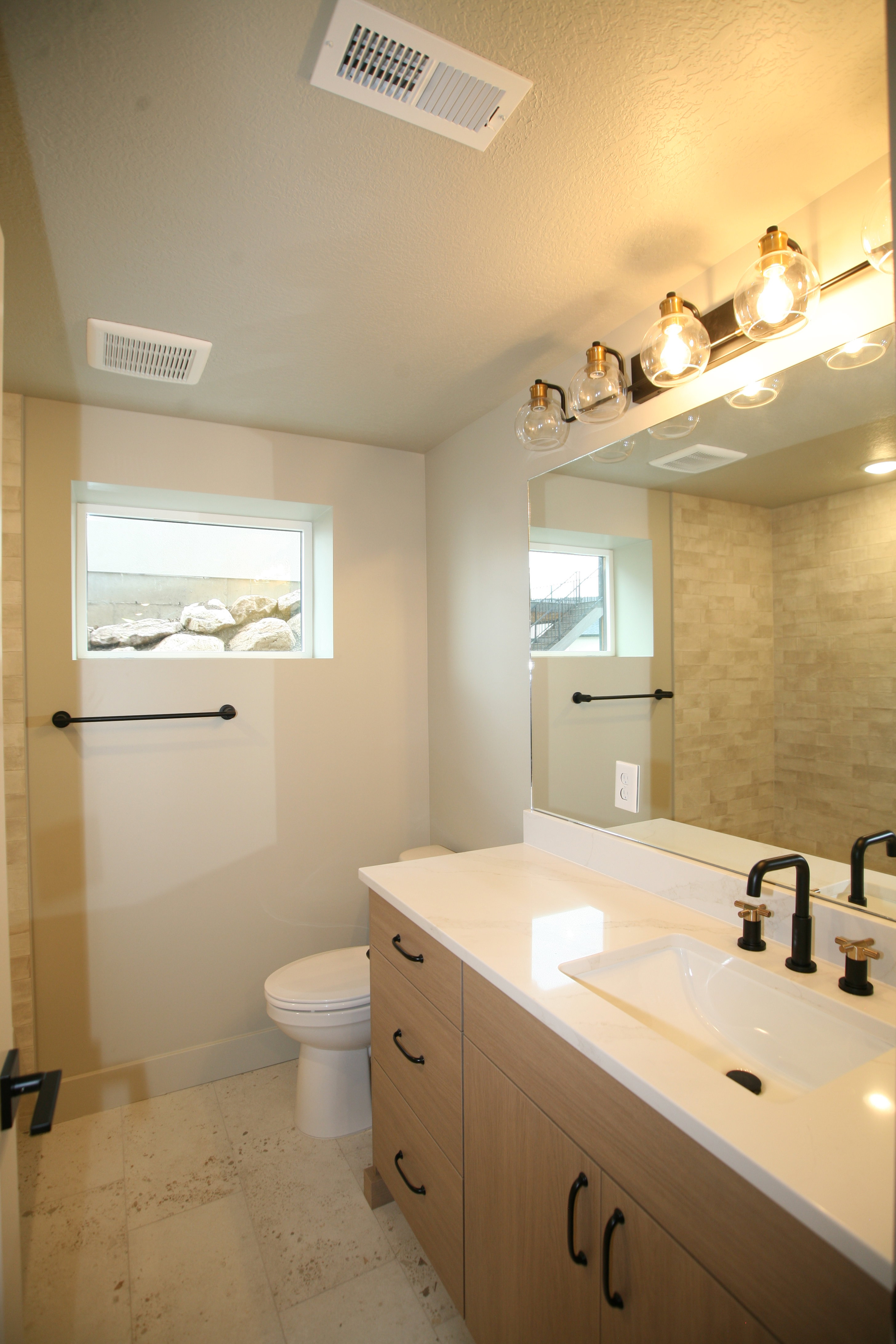 Bathroom featuring a wood-finish vanity with a light-colored countertop, an undermount sink, and a black faucet with gold accents