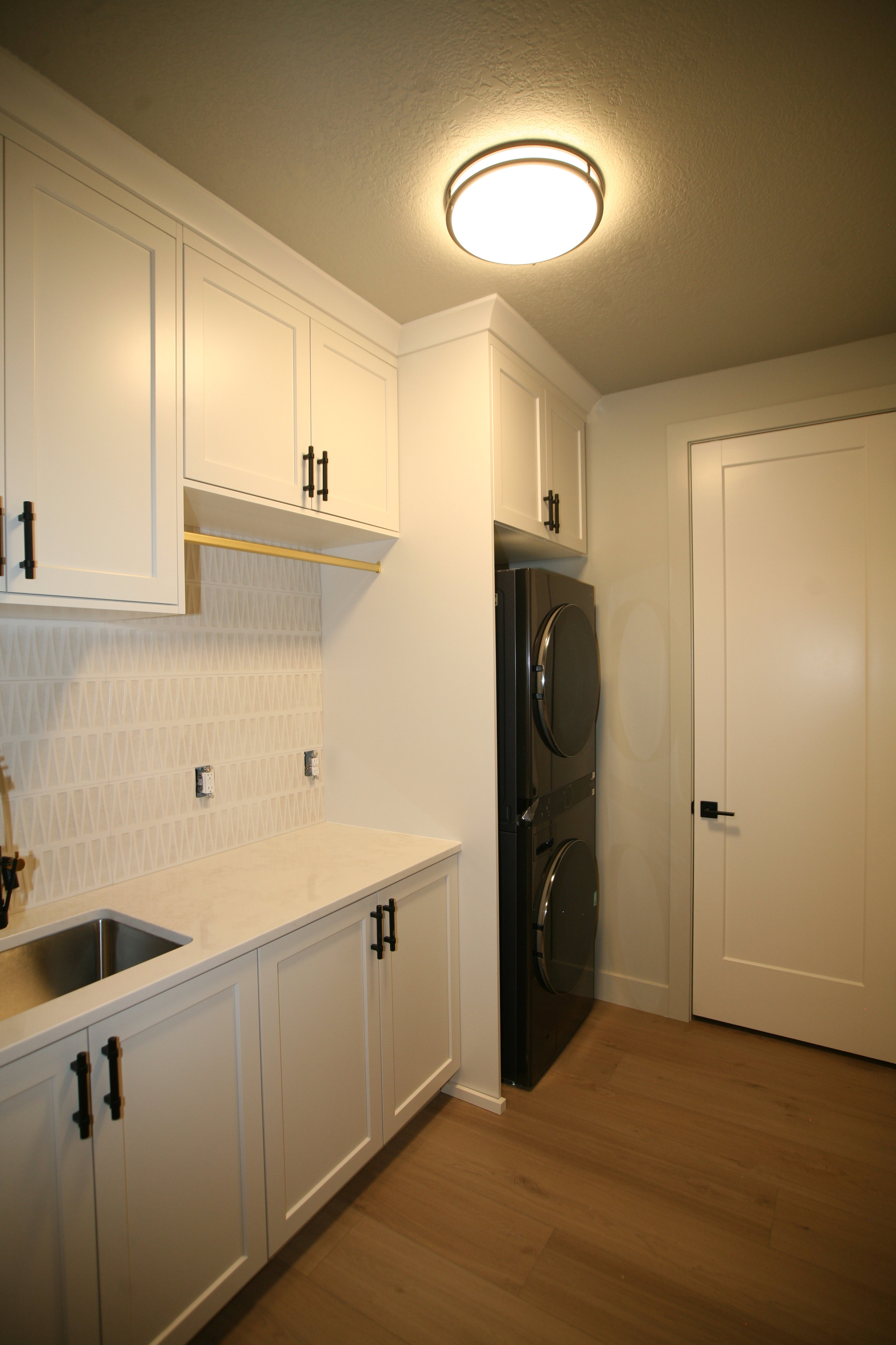 Laundry room featuring white shaker cabinetry, an integrated stainless steel utility sink, light-toned countertop, and a decorative tile backsplash