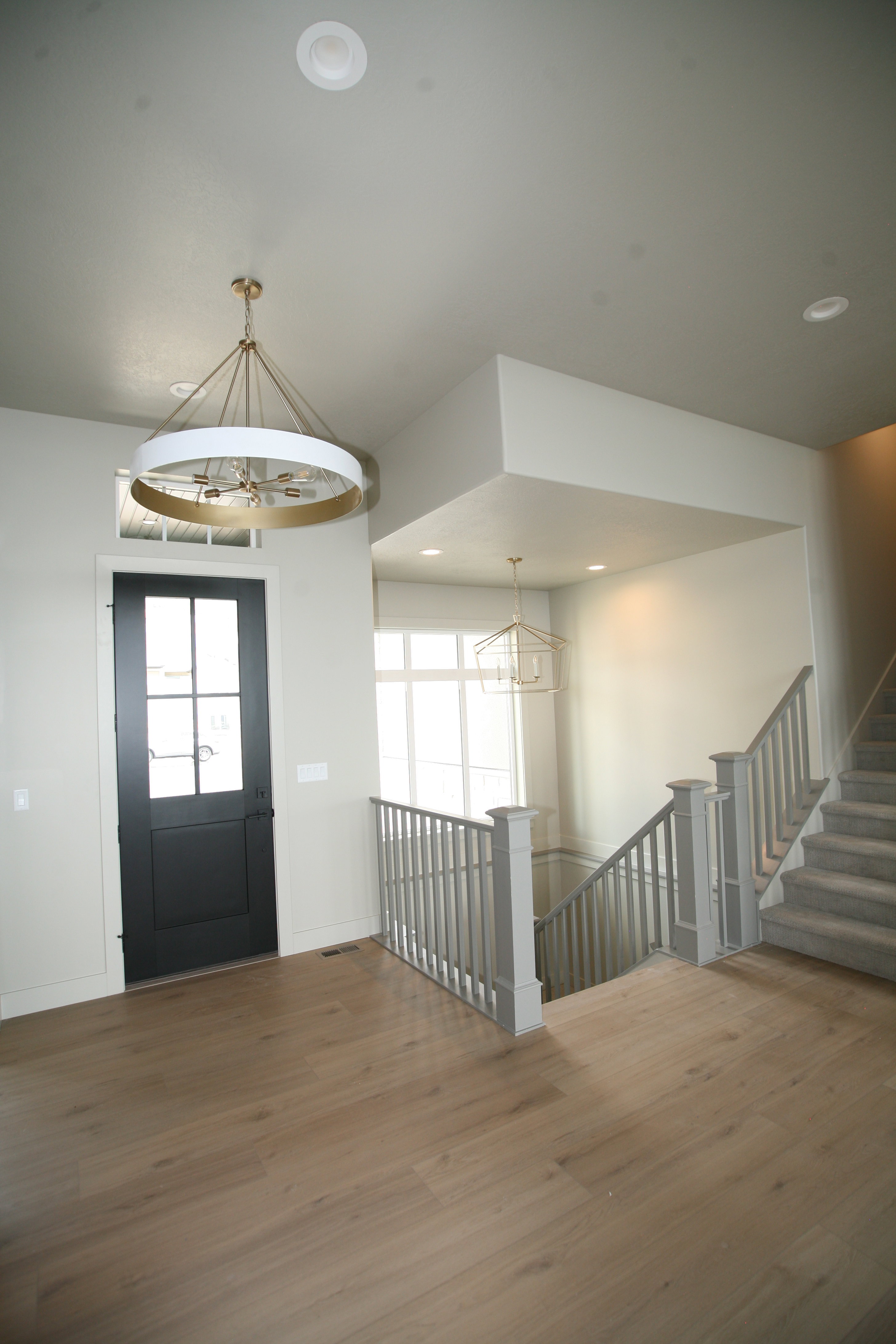 Entryway featuring wood-finish flooring, a dark-paneled front door with divided lites, and a chandelier with a gold-tone frame and white drum shade