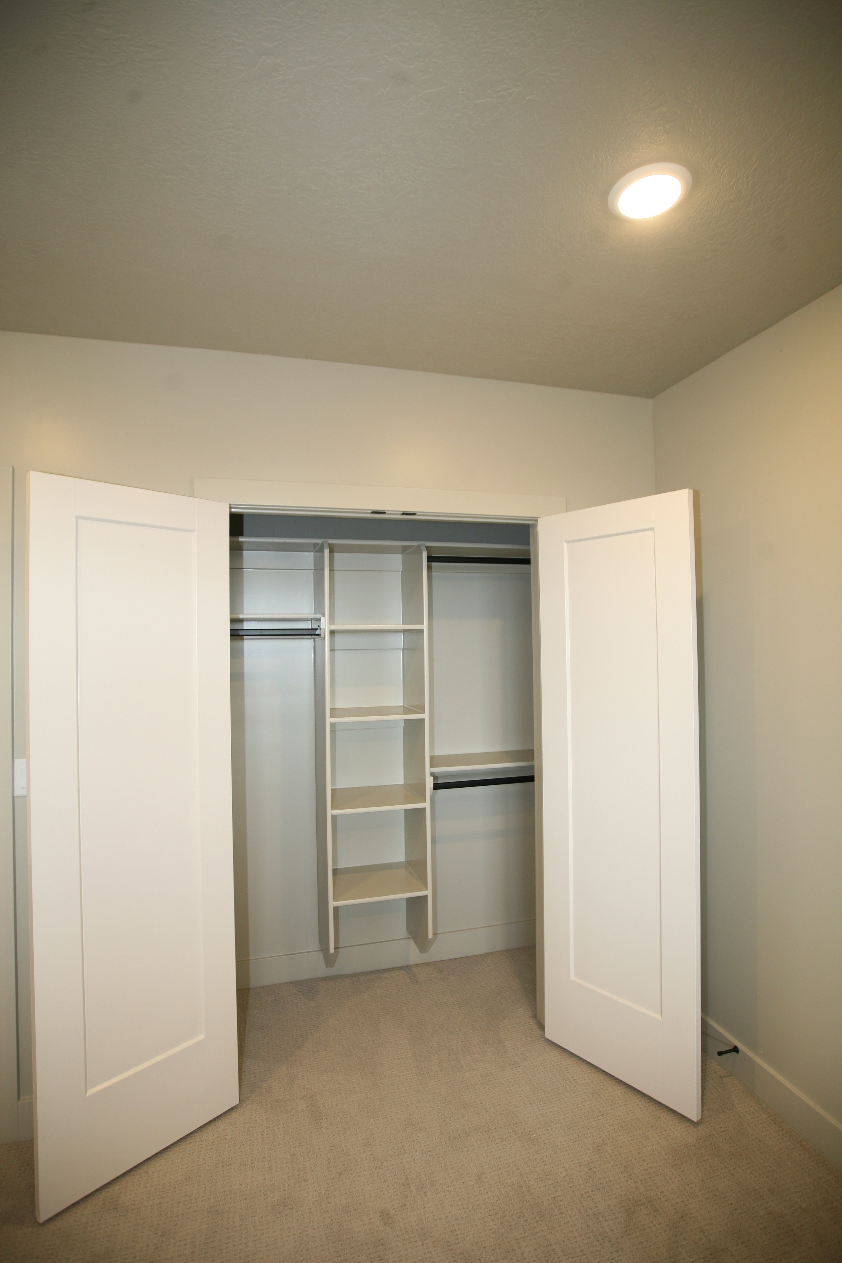 Closet with bi-fold doors, built-in shelving, two clothing rods, and recessed lighting