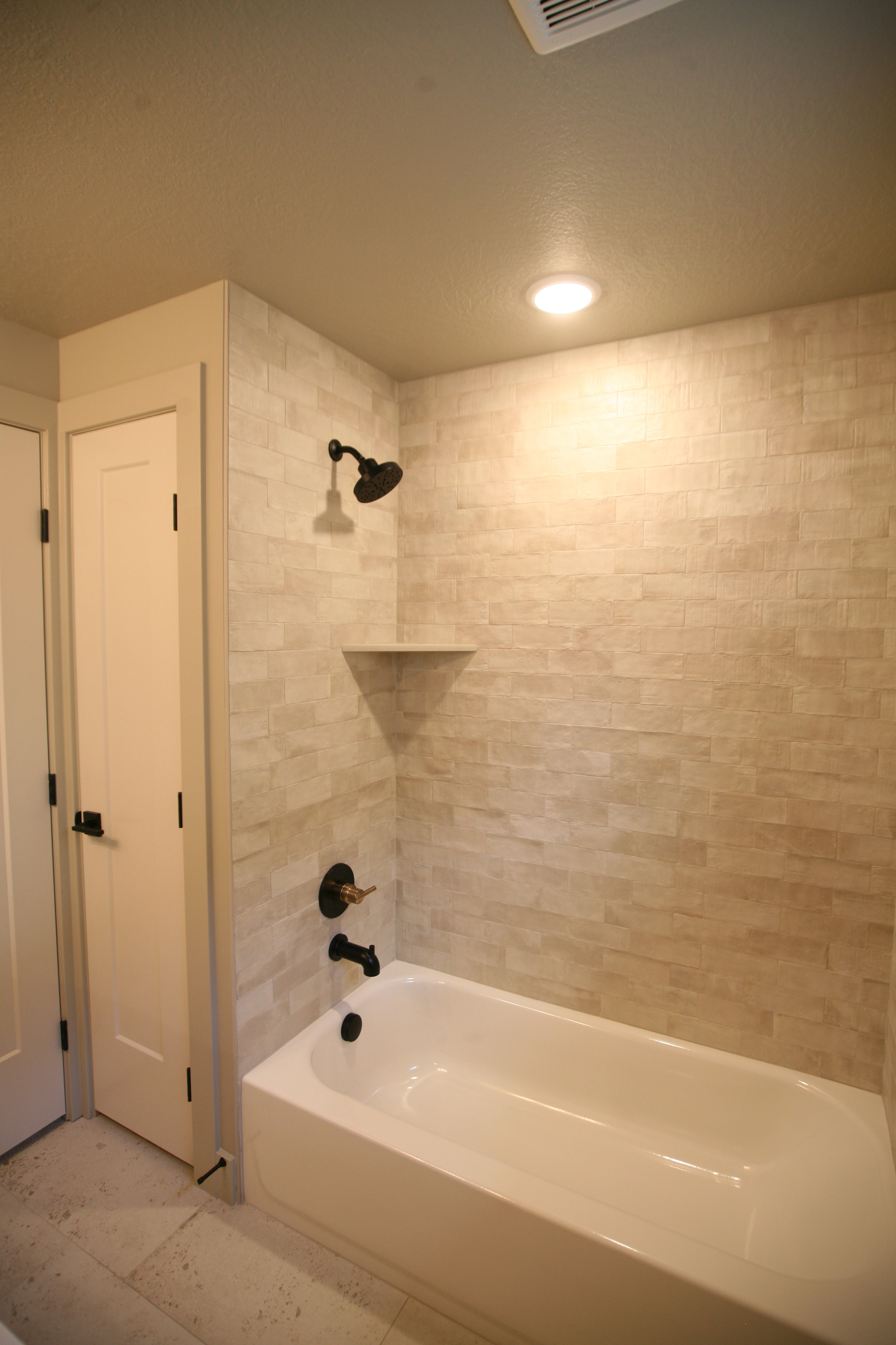 Bathtub and shower combination featuring stacked rectangular wall tile and matte black fixtures