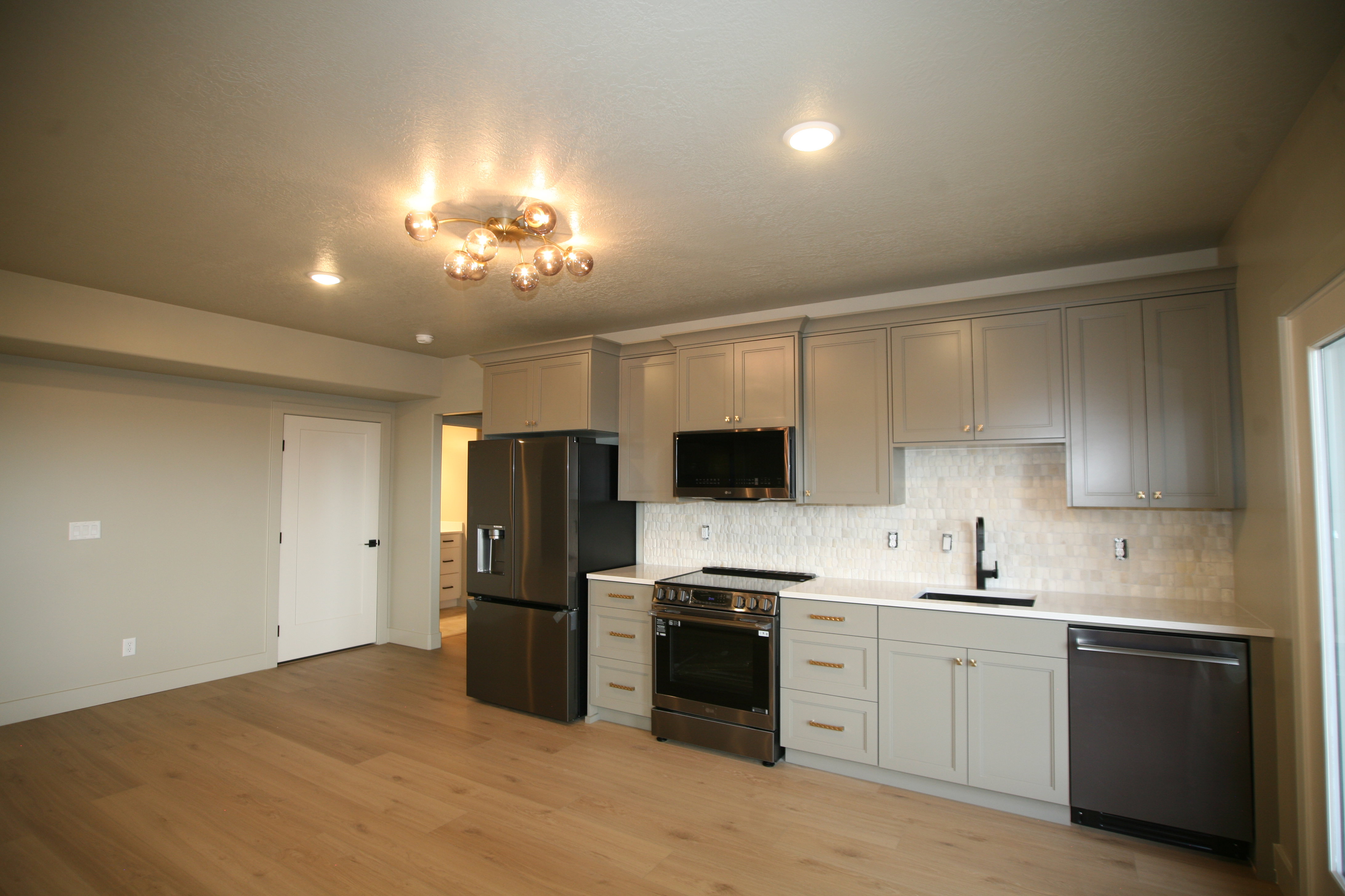 Modern kitchen featuring light gray cabinetry, white countertops, stainless steel appliances, and wood-finish flooring