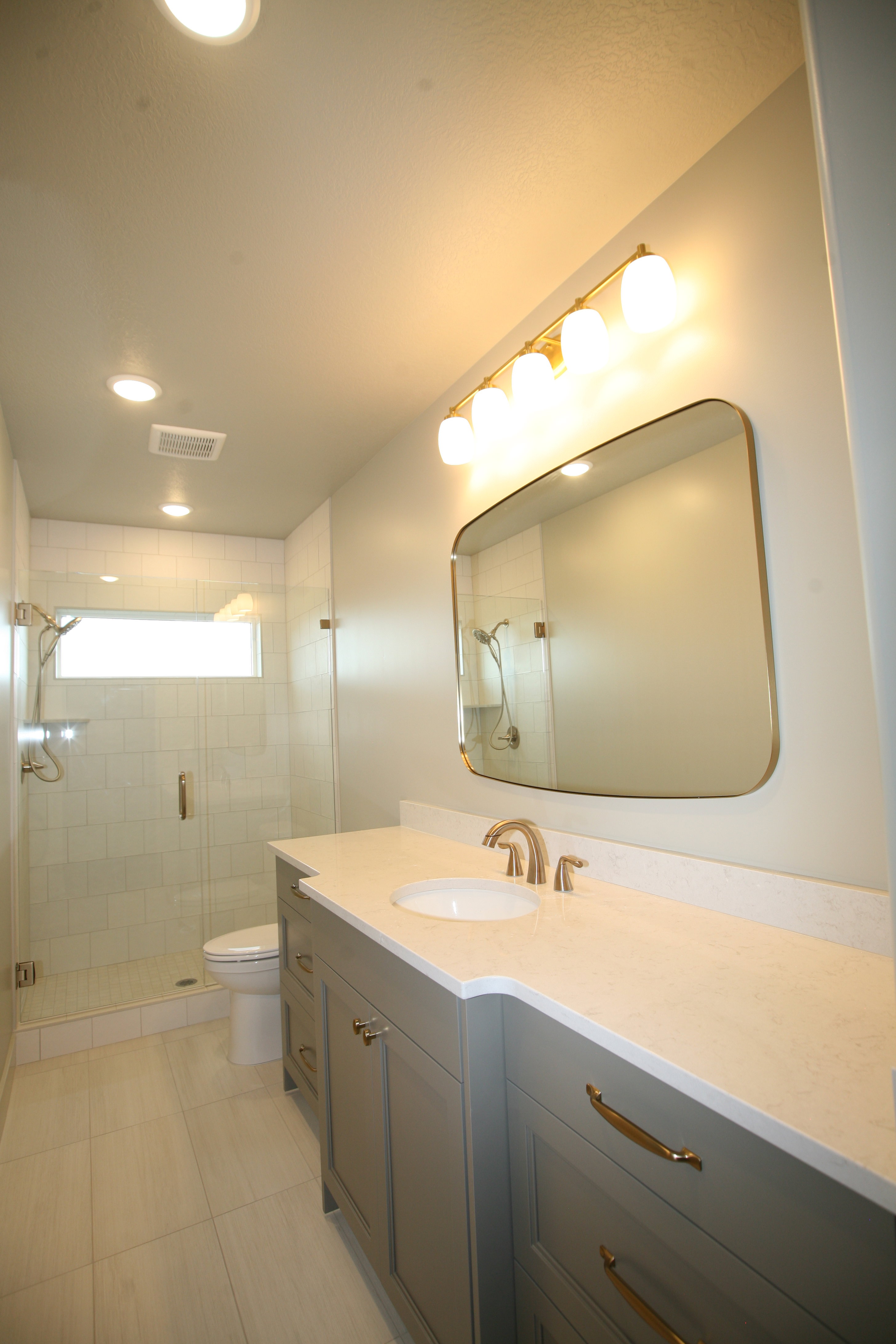 Contemporary bathroom featuring a spacious vanity with an undermount sink and light-toned countertop, a frameless mirror, and a glass-enclosed shower with subway tile surround and a transom window