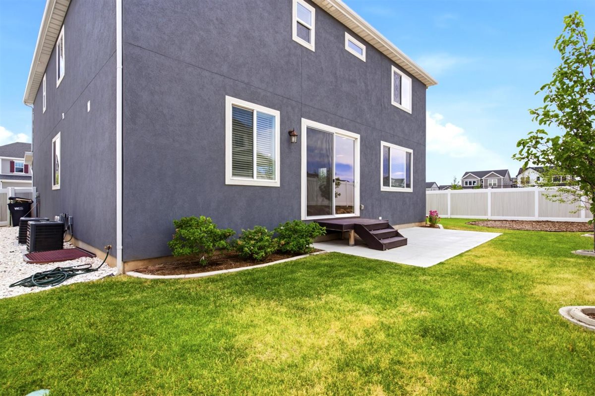 Rear exterior showcasing a concrete patio with wood-finish steps, a sliding glass door, and a white vinyl privacy fence