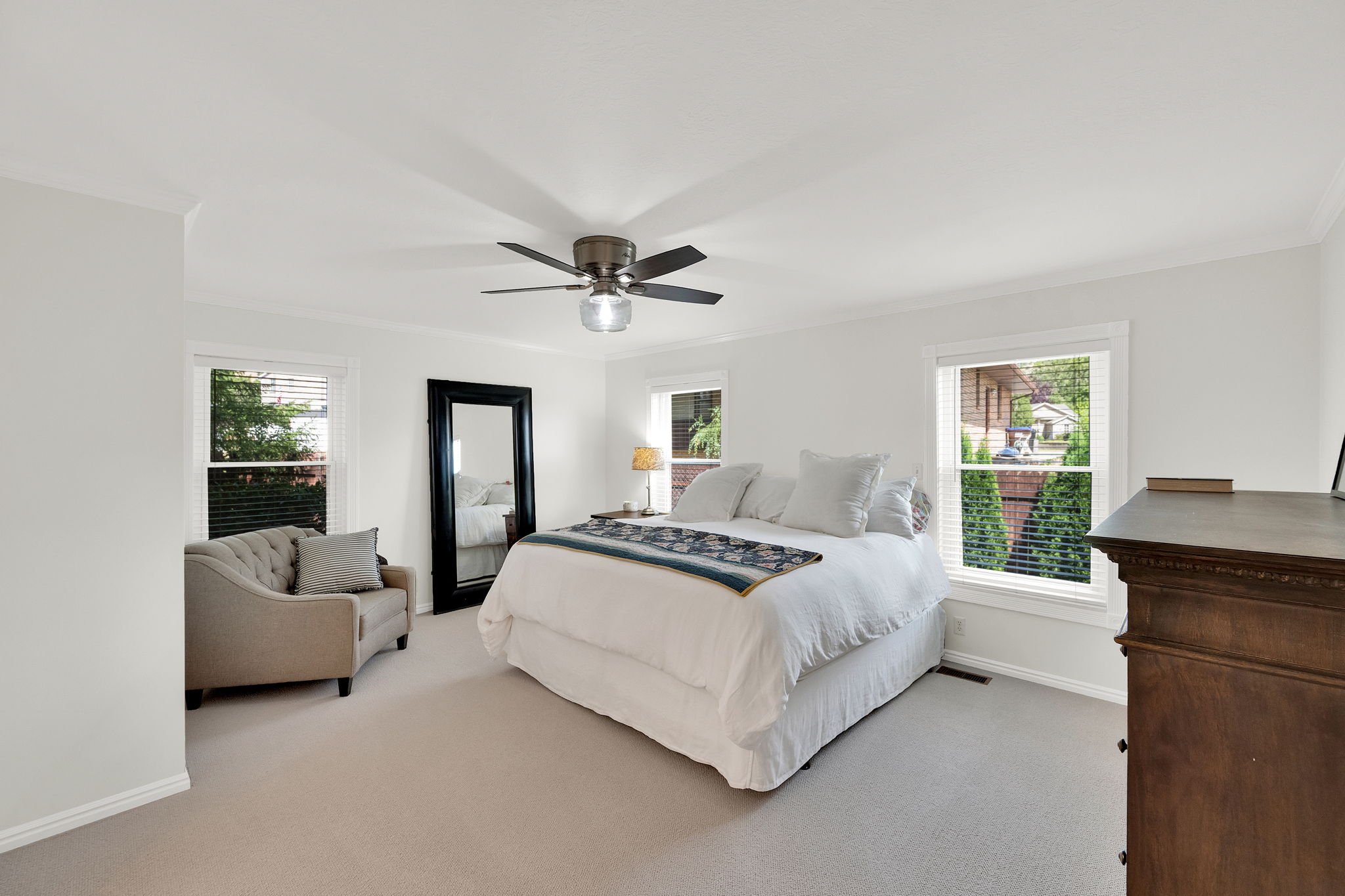 Spacious primary suit featuring light-colored carpeting, multiple windows with blinds, a ceiling fan with integrated lighting, and crown molding
