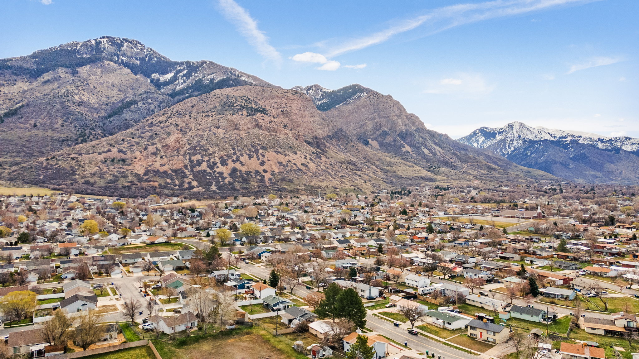 Expansive residential area with a mountain backdrop, featuring a clear sky, mature trees, and a mix of single-story and multi-story homes