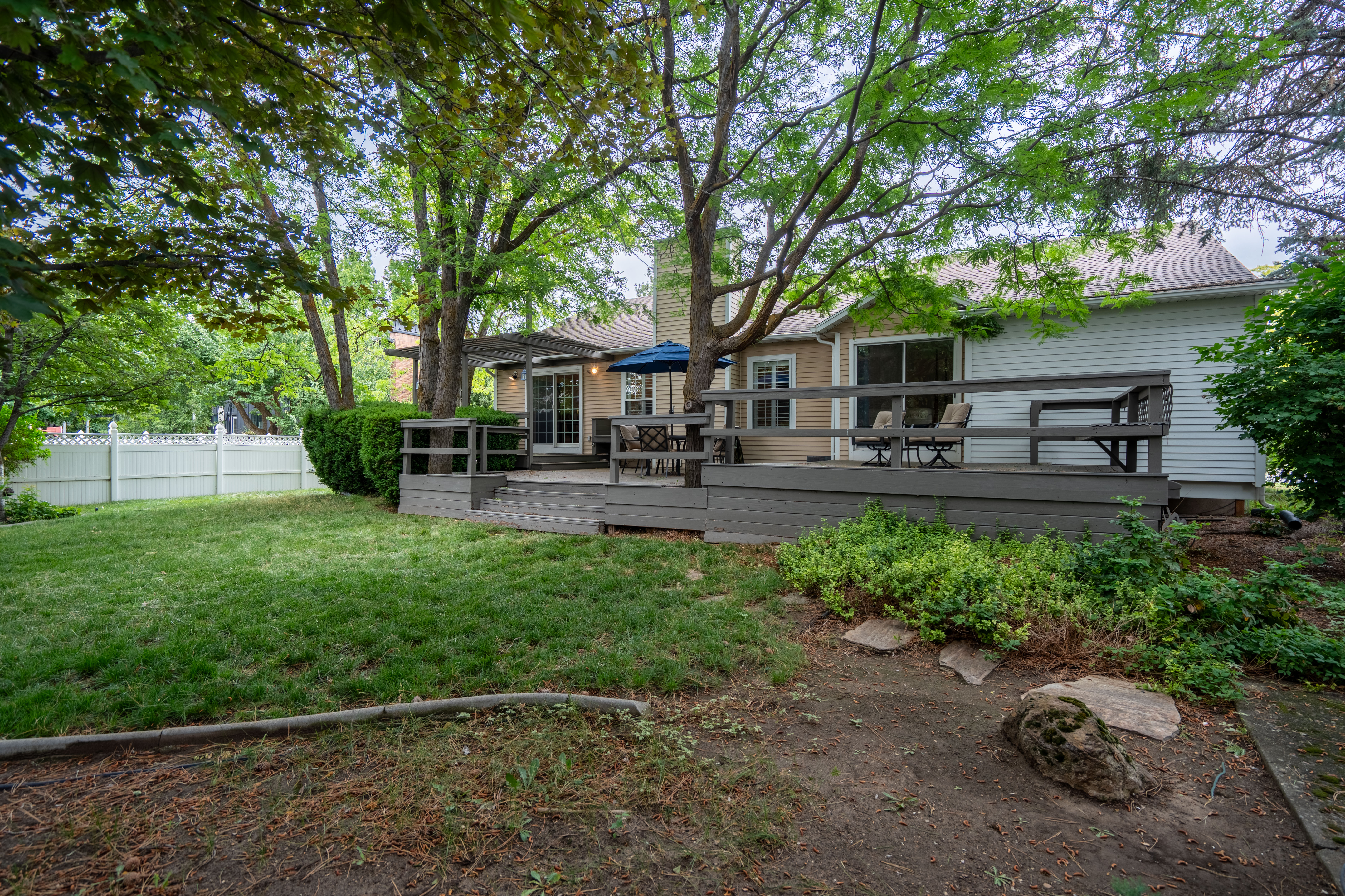 Expansive backyard featuring a multi-level deck, mature trees, a white perimeter fence, and sliding glass door access to the interior