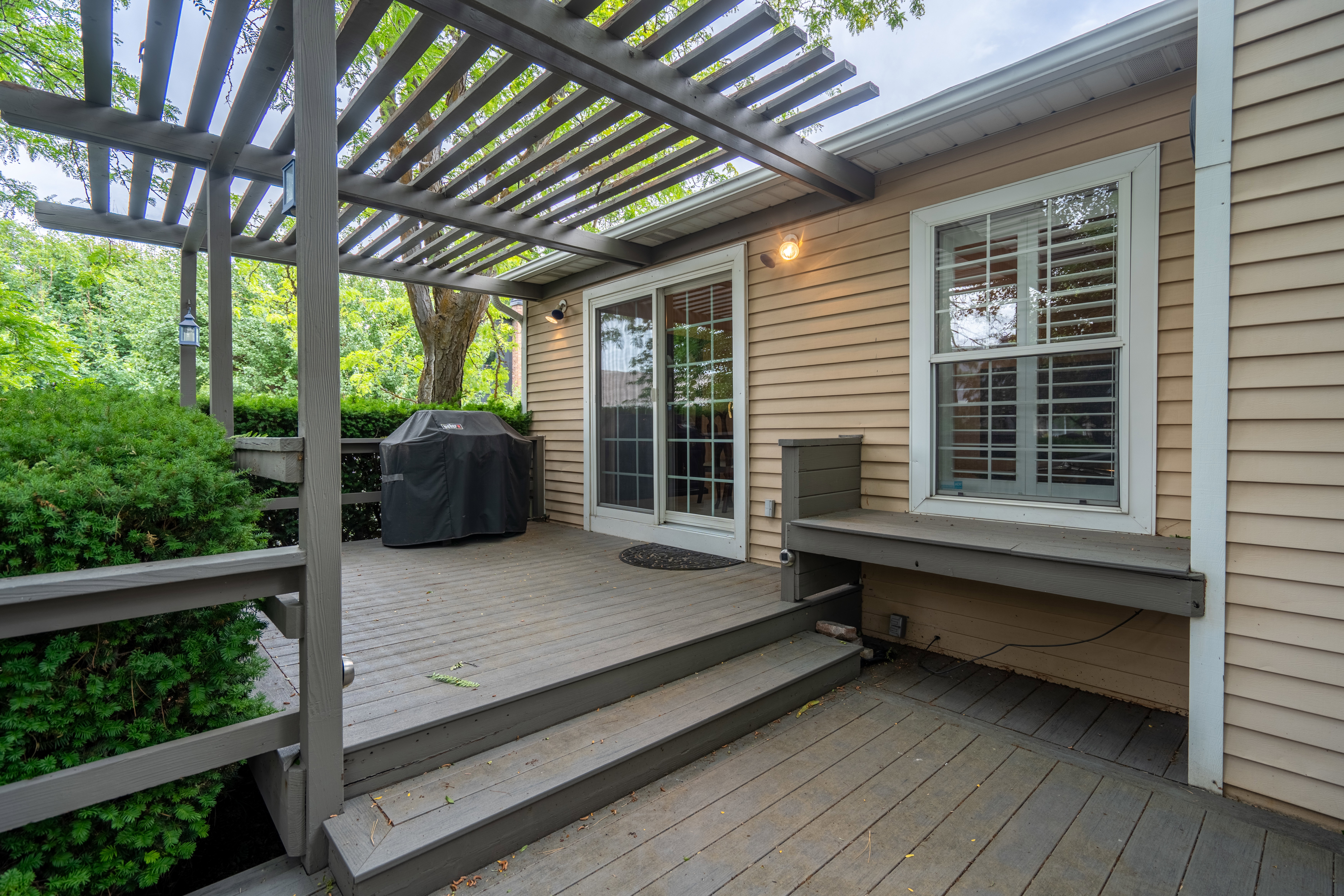 Expansive outdoor deck featuring a slatted pergola, built-in bench seating, and wood-finish siding