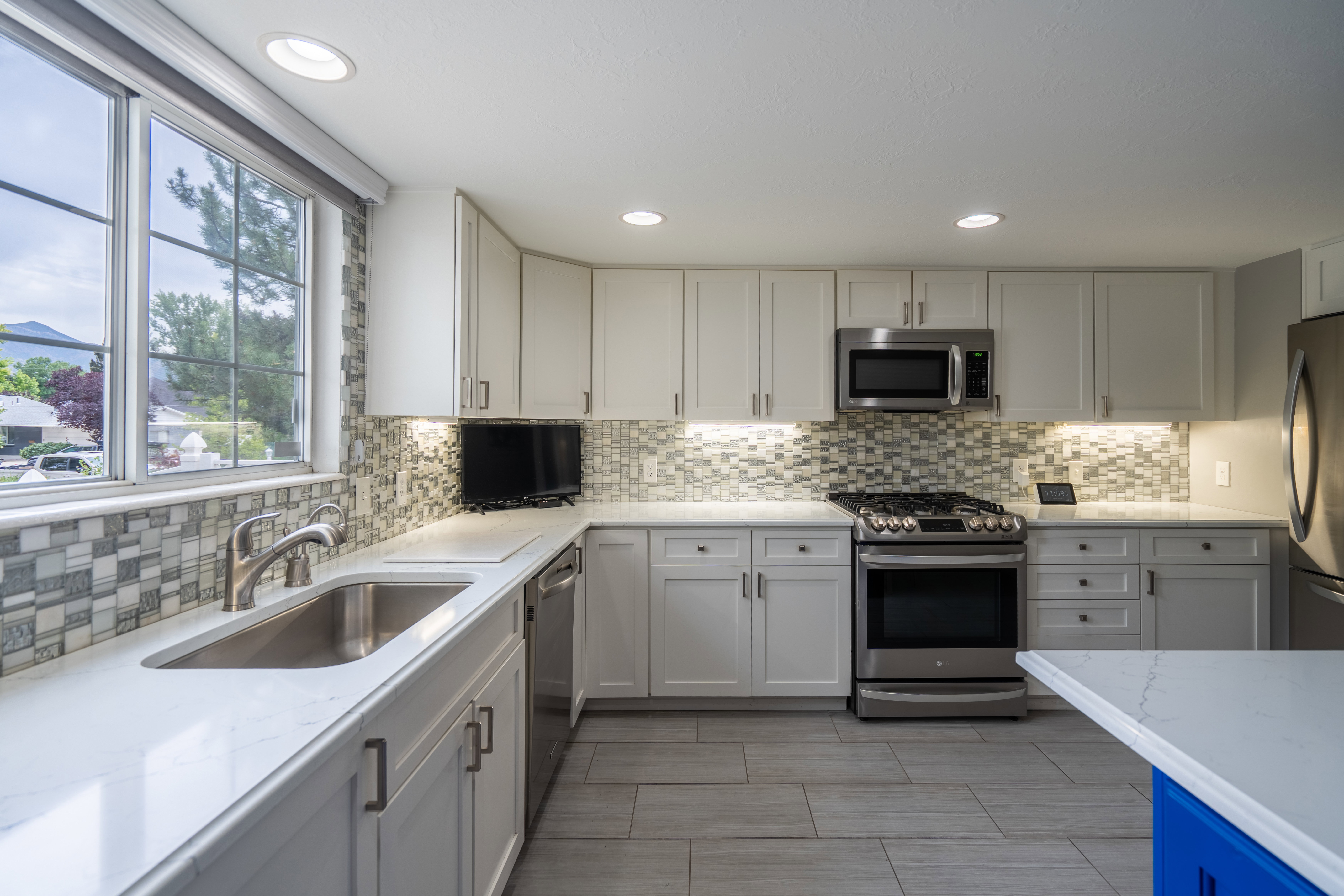 Modern kitchen featuring white shaker cabinetry, stainless steel appliances, mosaic tile backsplash, and light-toned countertops