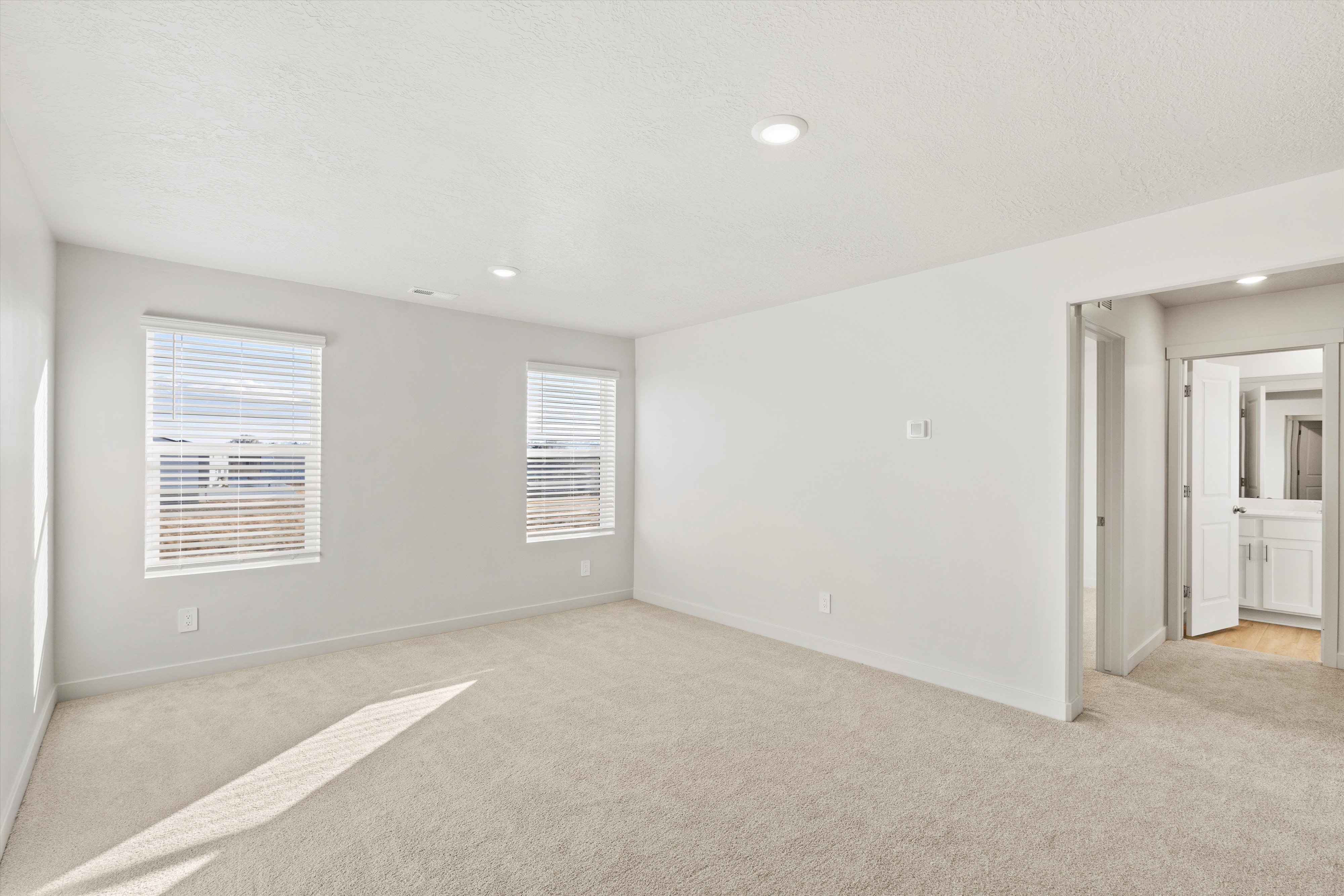 Carpeted room with recessed lighting and two windows featuring horizontal blinds
