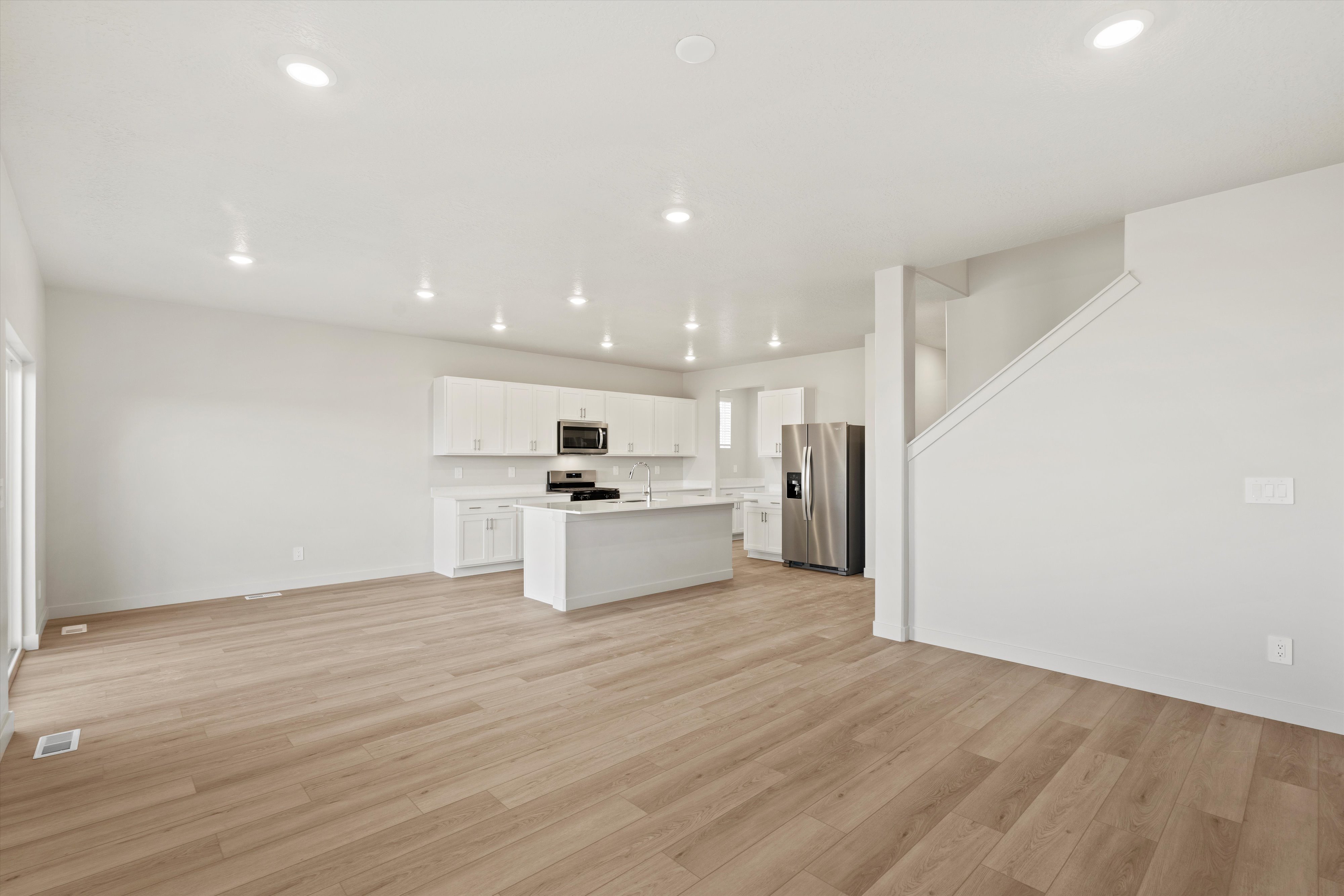 Open-concept living space featuring wood-finish flooring, recessed lighting, and a white kitchen with stainless steel appliances