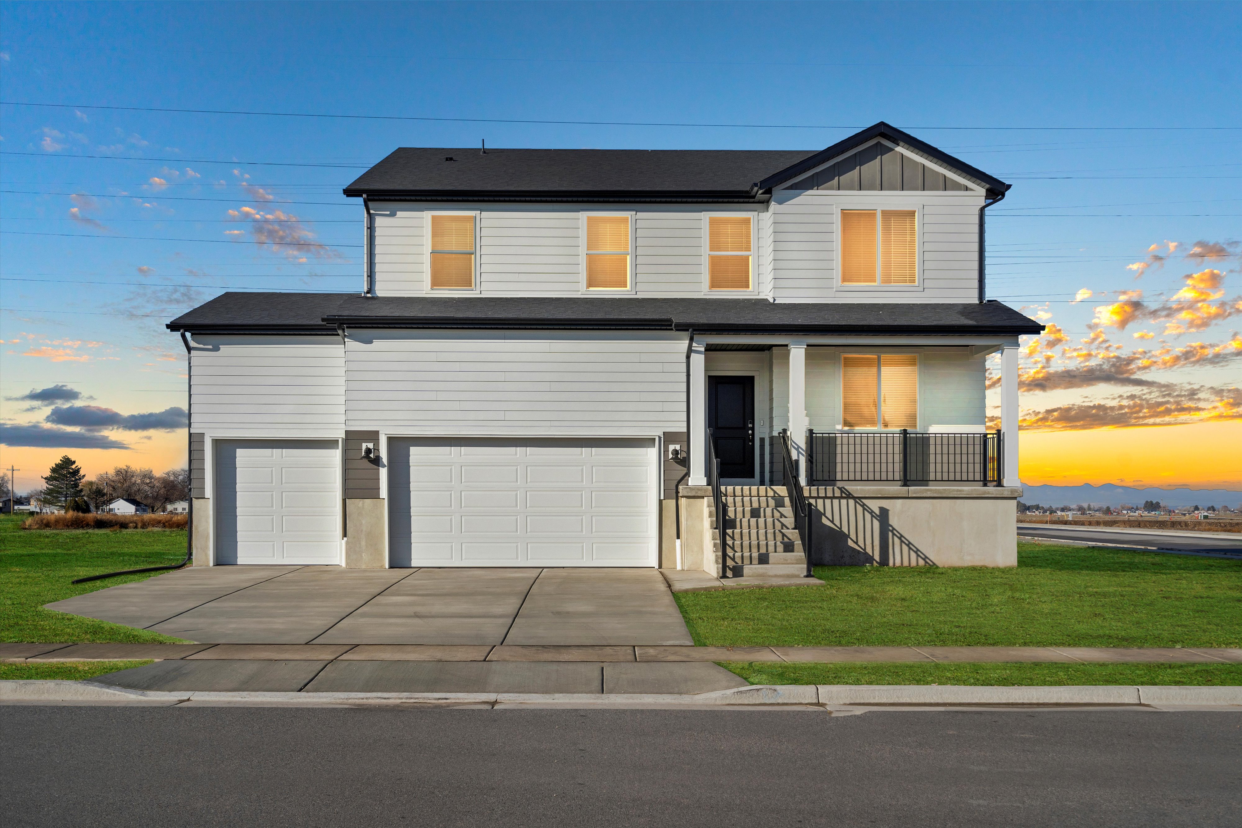 Two-story residence featuring a covered front porch, a two-car garage, and light-colored siding with dark trim accents