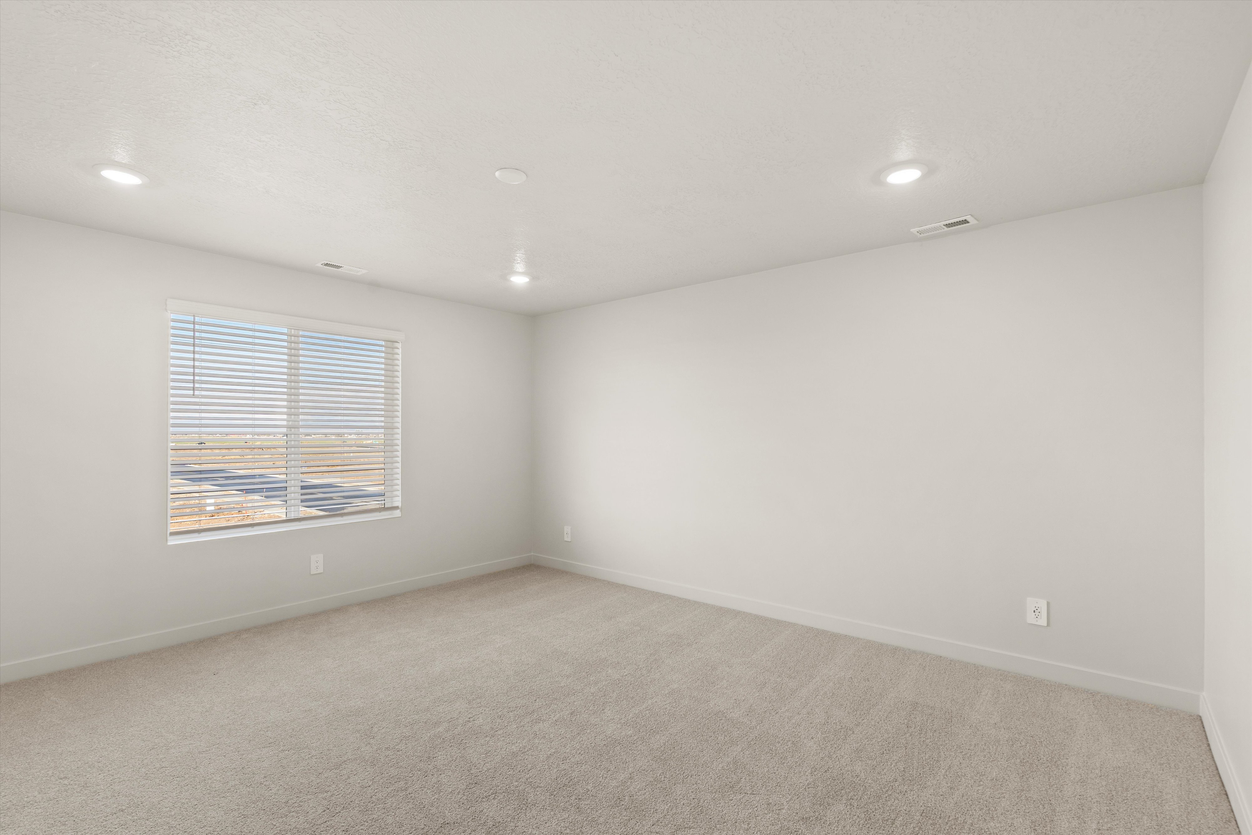 Spacious room featuring neutral carpeting, light-toned walls, and recessed lighting
