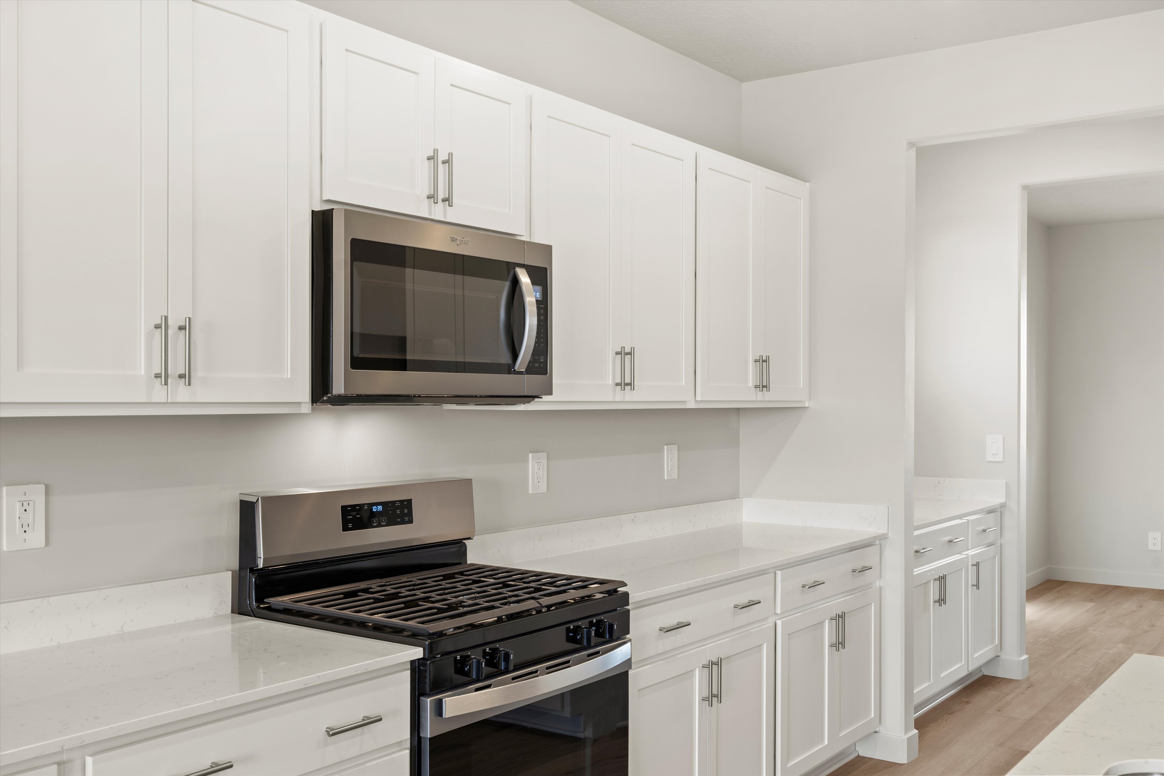 Modern kitchen featuring white shaker cabinetry, stainless steel range and microwave, light-toned countertops, and light wood-finish flooring