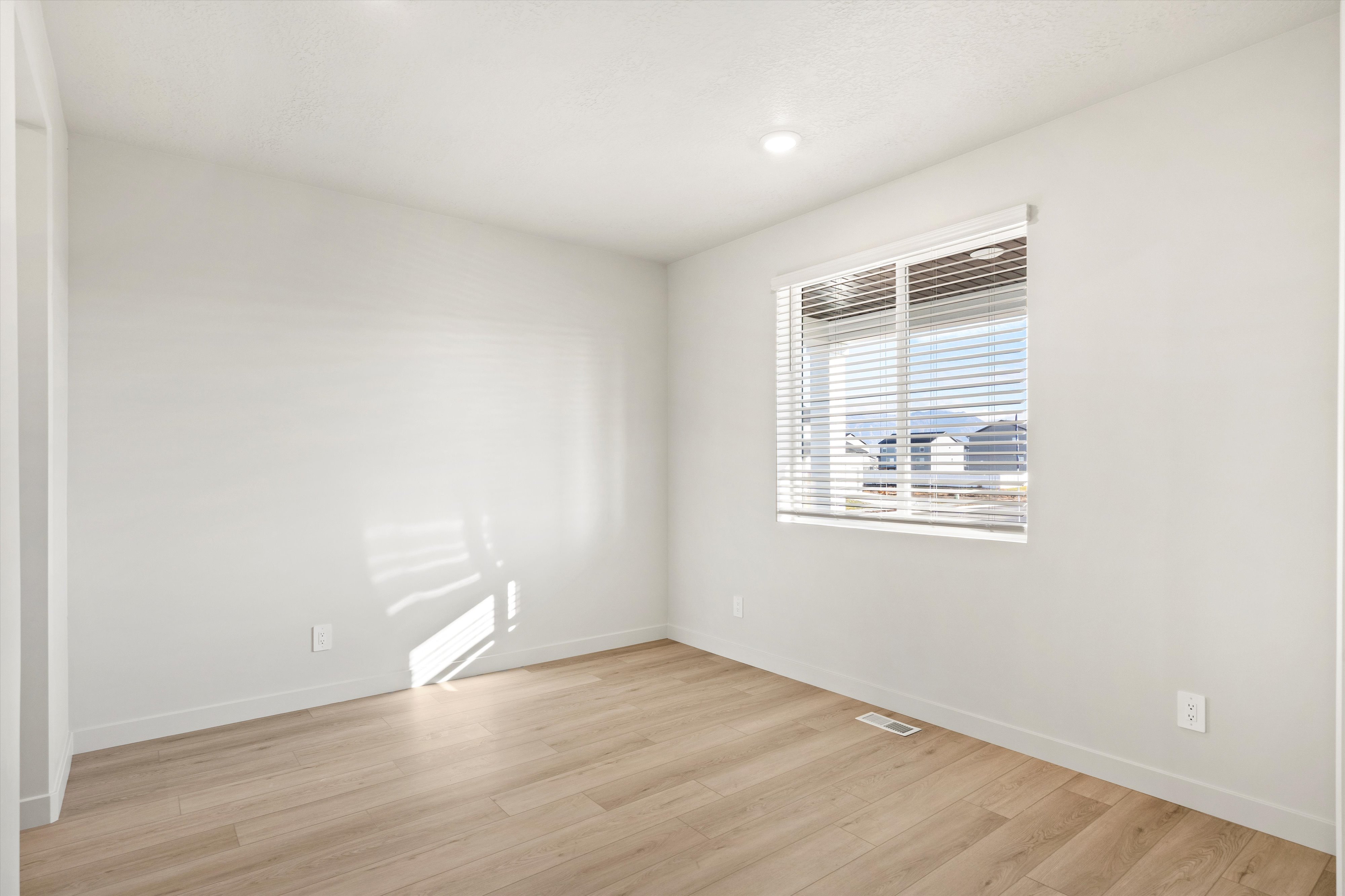 Bright room featuring a large window with horizontal blinds, wood-finish flooring, white walls, and recessed lighting