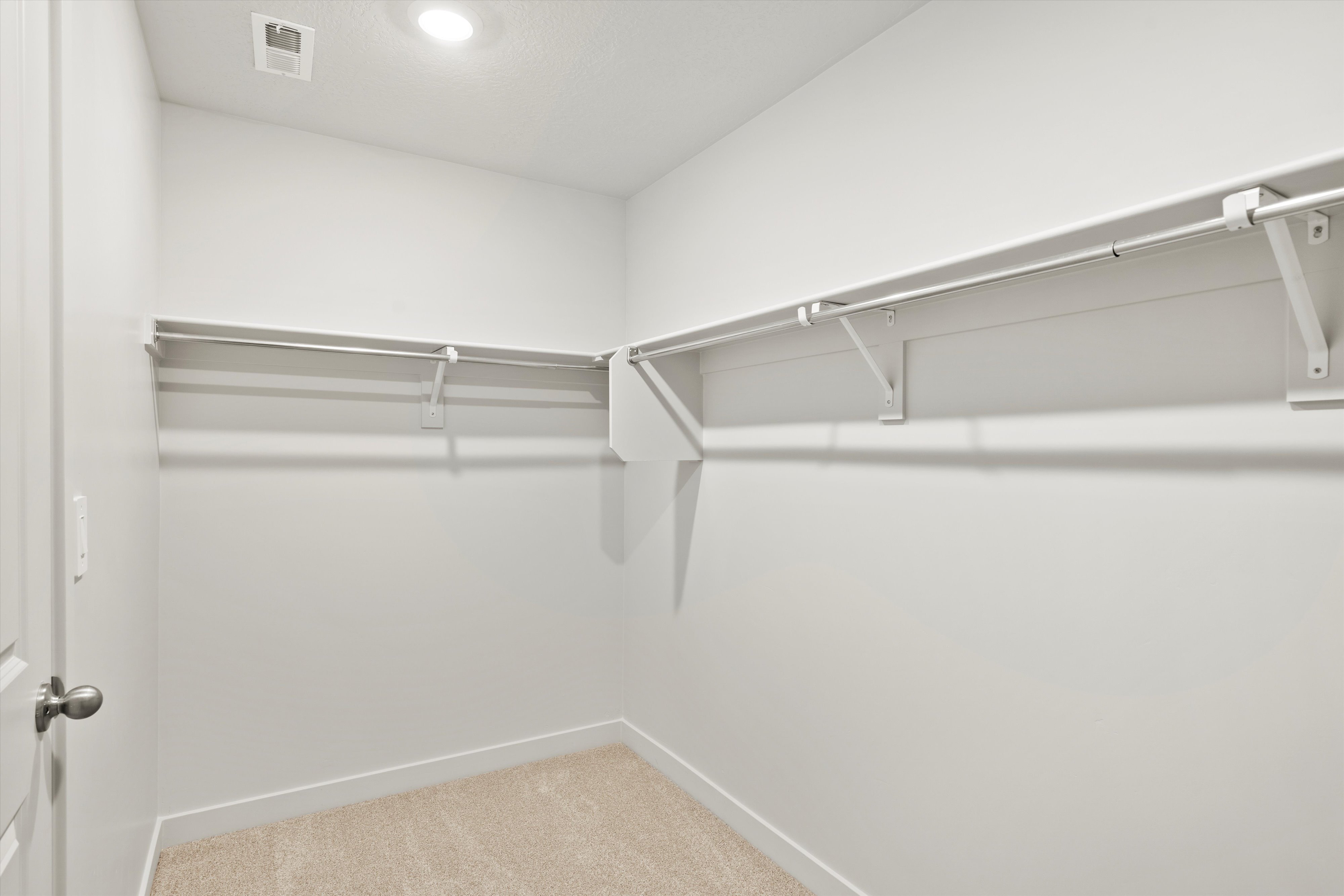 Walk-in closet featuring light-colored carpeting, white baseboards, and built-in white shelving with hanging rods