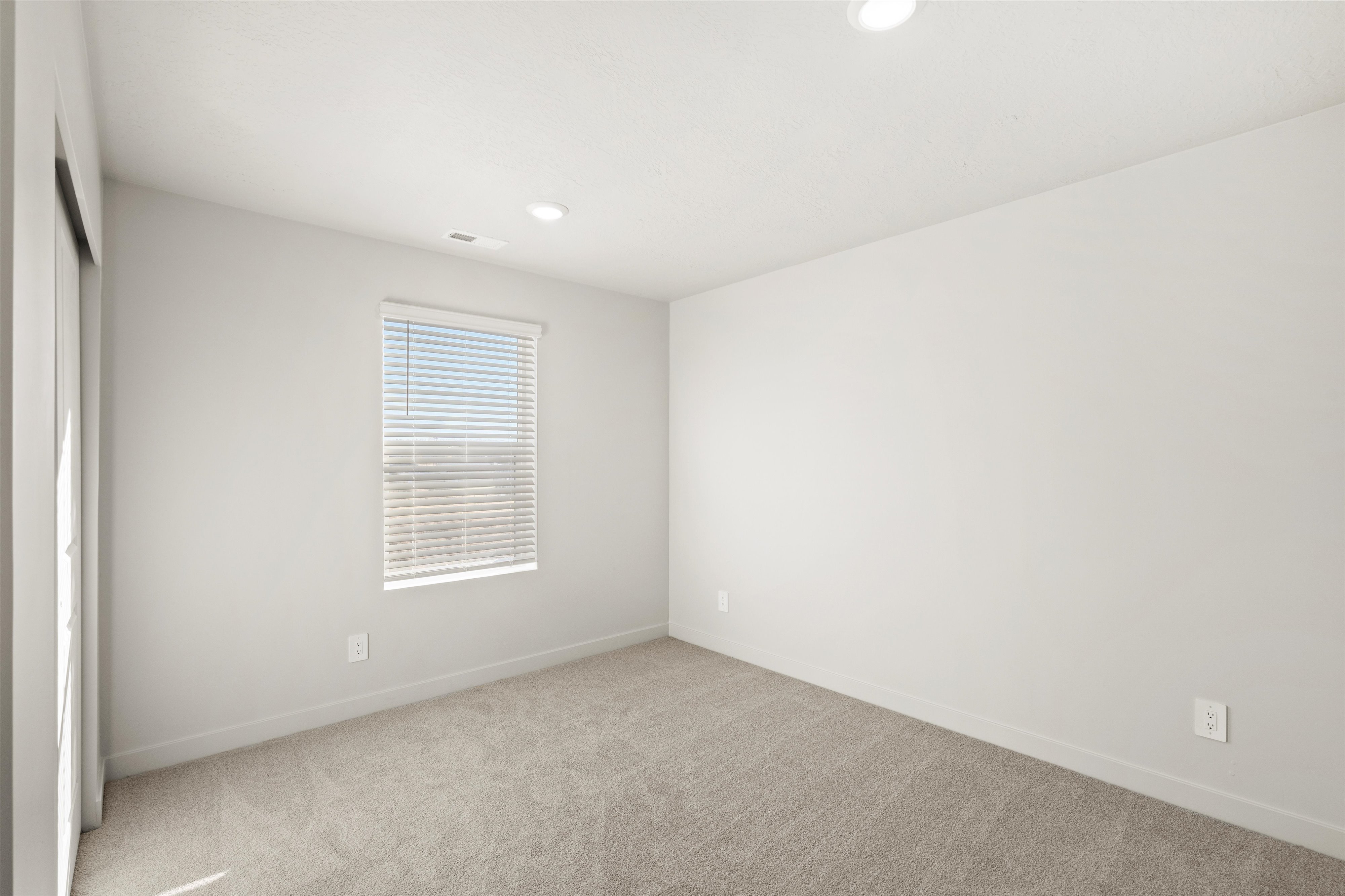 Carpeted room featuring a single window with horizontal blinds, recessed ceiling lighting, and light gray wall paint