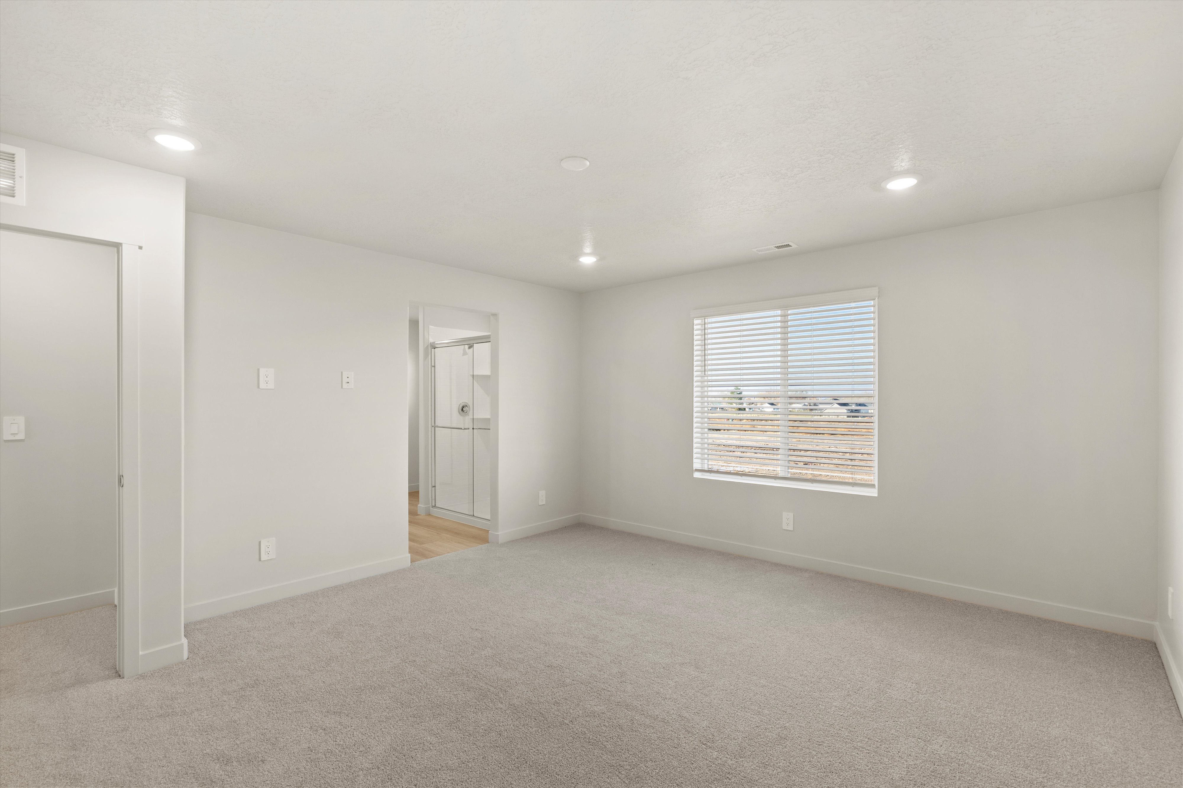 Carpeted room with recessed lighting and a large window featuring horizontal blinds