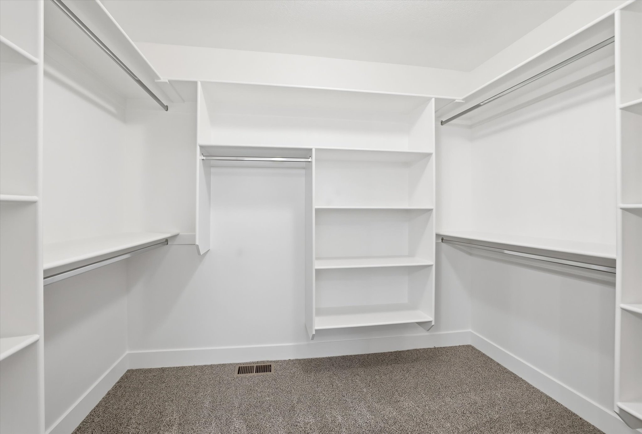Expansive walk-in closet featuring white built-in shelving, multiple hanging rods, and light gray carpeting