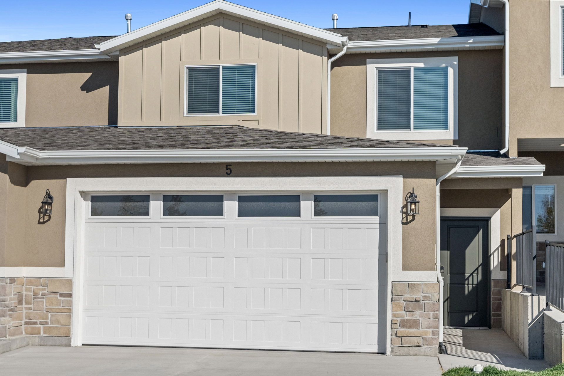 Exterior featuring a two-car garage with transom windows, a stone facade accent, and decorative exterior lighting