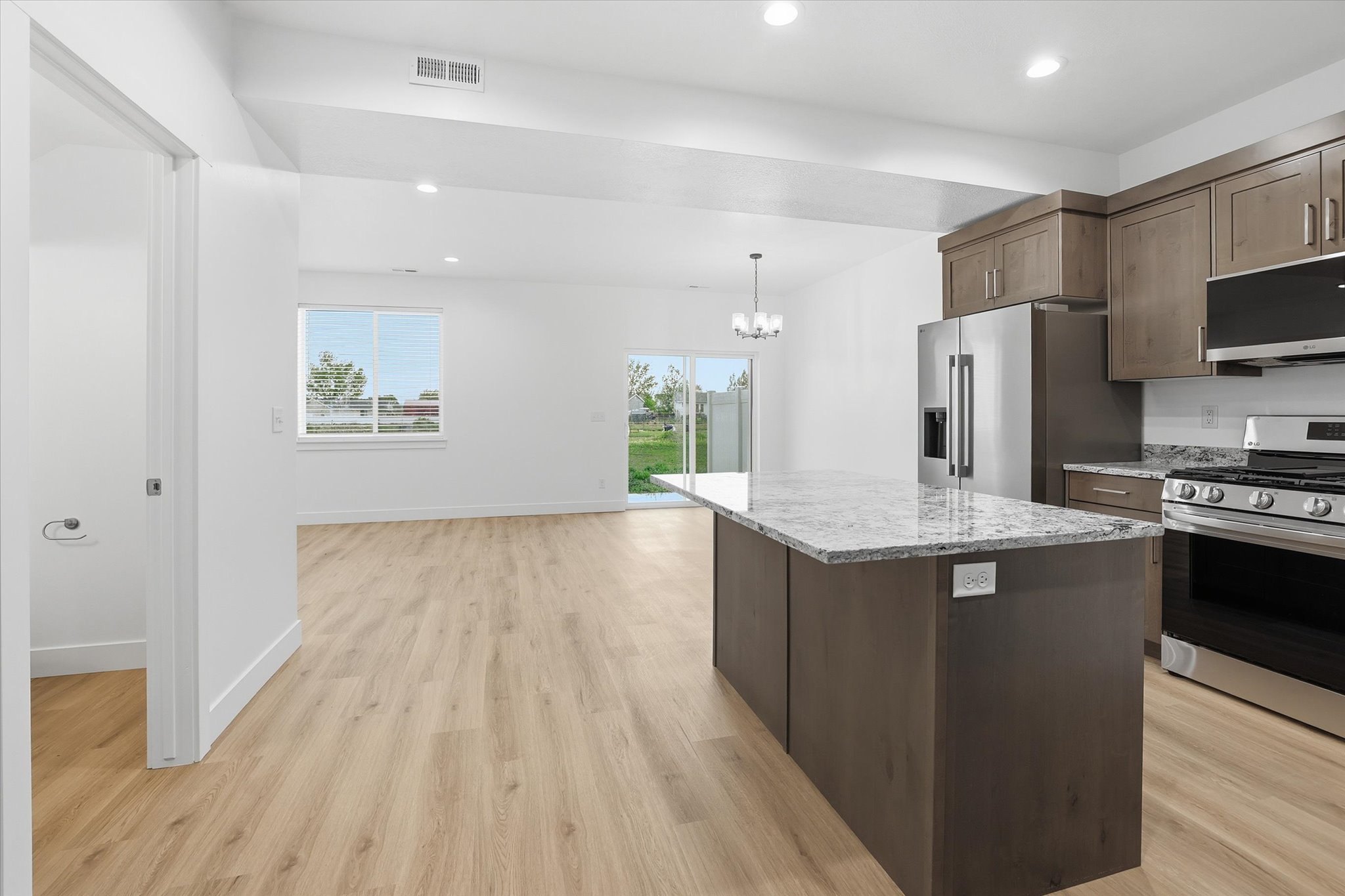 Spacious kitchen featuring a large island with a light-toned countertop, stainless steel appliances, wood-finish flooring, and white cabinetry