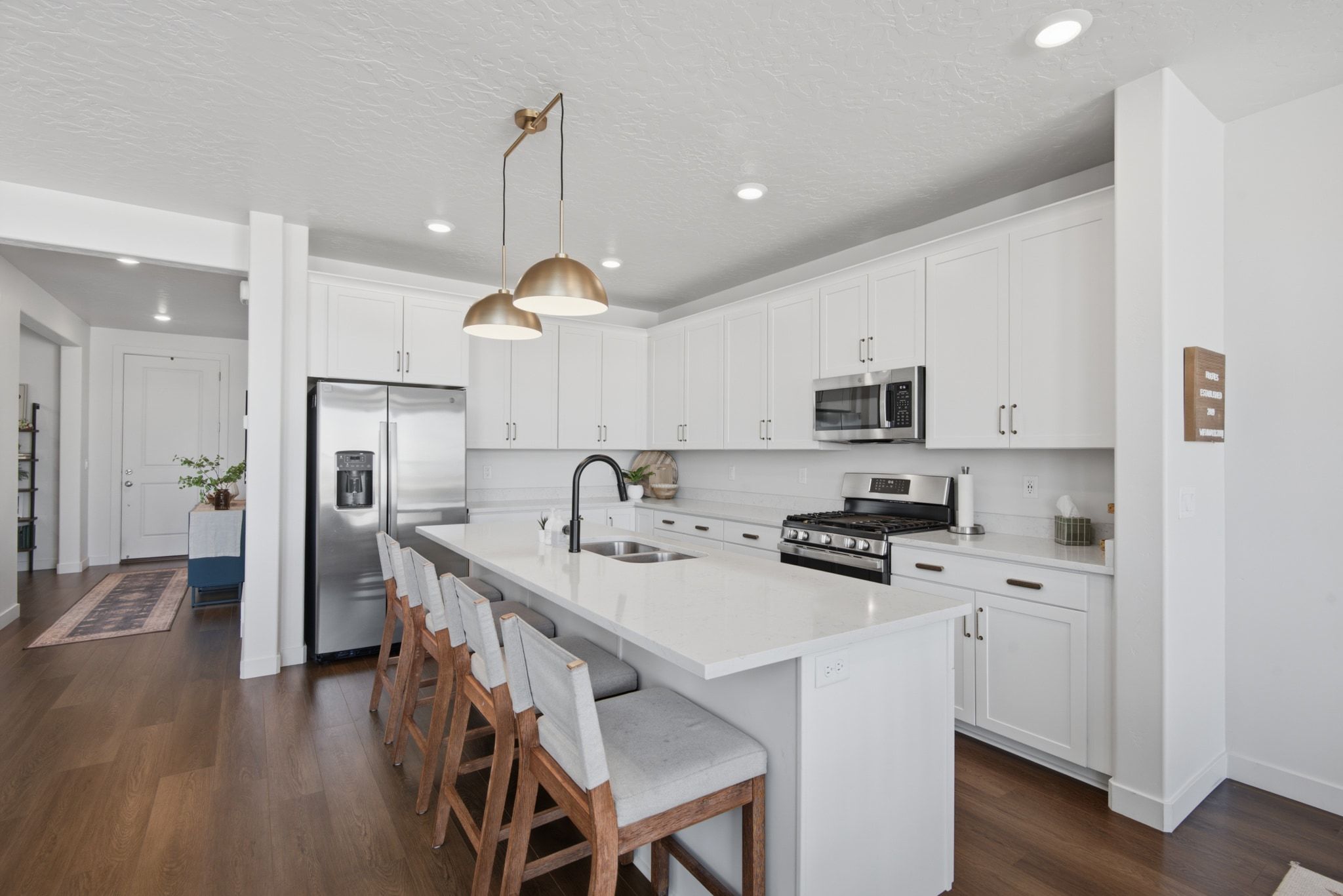 Contemporary kitchen featuring a large central island with seating, white shaker-style cabinetry, stainless steel appliances, and wood-finish flooring