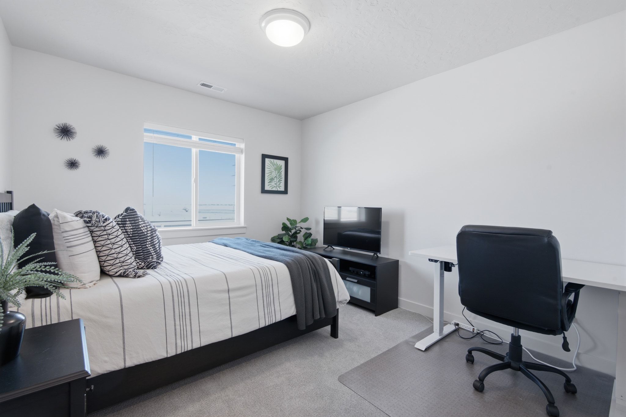 Well-lit room featuring neutral wall tones, light gray carpet, and a prominent window