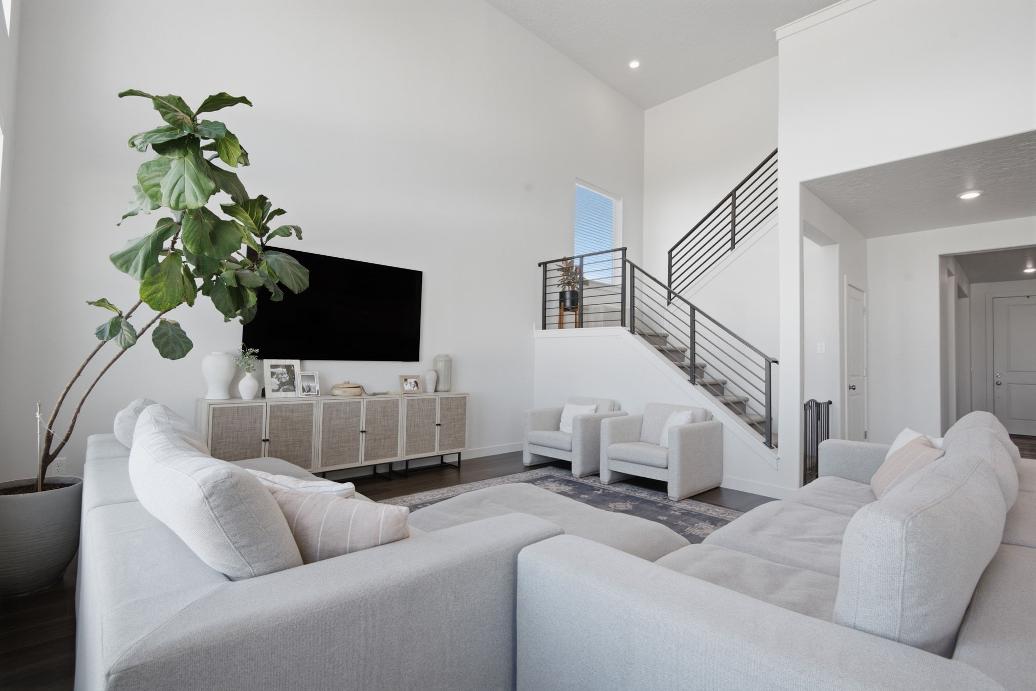 Two-story living area featuring vaulted ceilings, dark wood-finish flooring, a contemporary staircase with black metal railings, and a built-in media console with woven doors