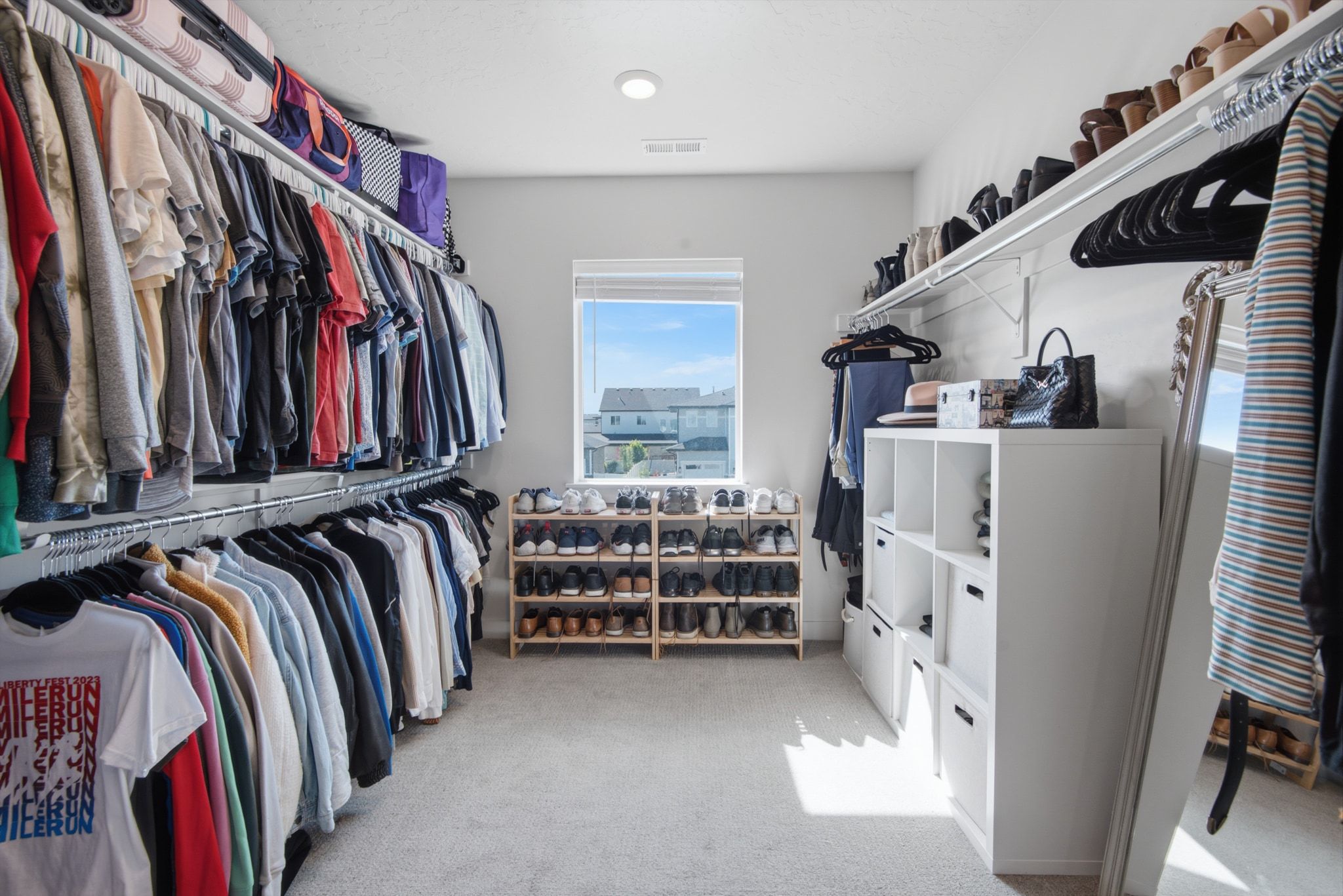 Spacious walk-in closet featuring extensive built-in shelving, hanging rods, an integrated window, and carpeted flooring