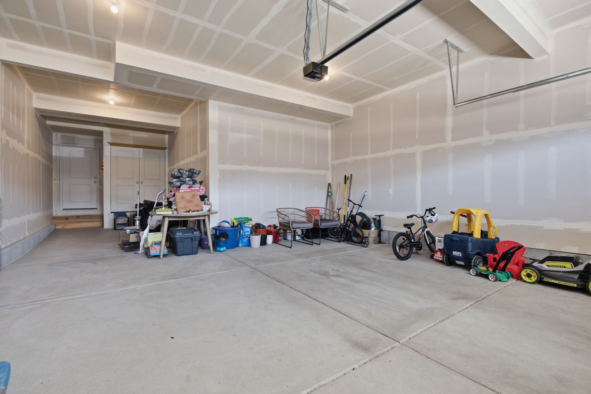 Spacious unfinished garage with concrete flooring, drywall-ready walls, and an overhead garage door opener mechanism