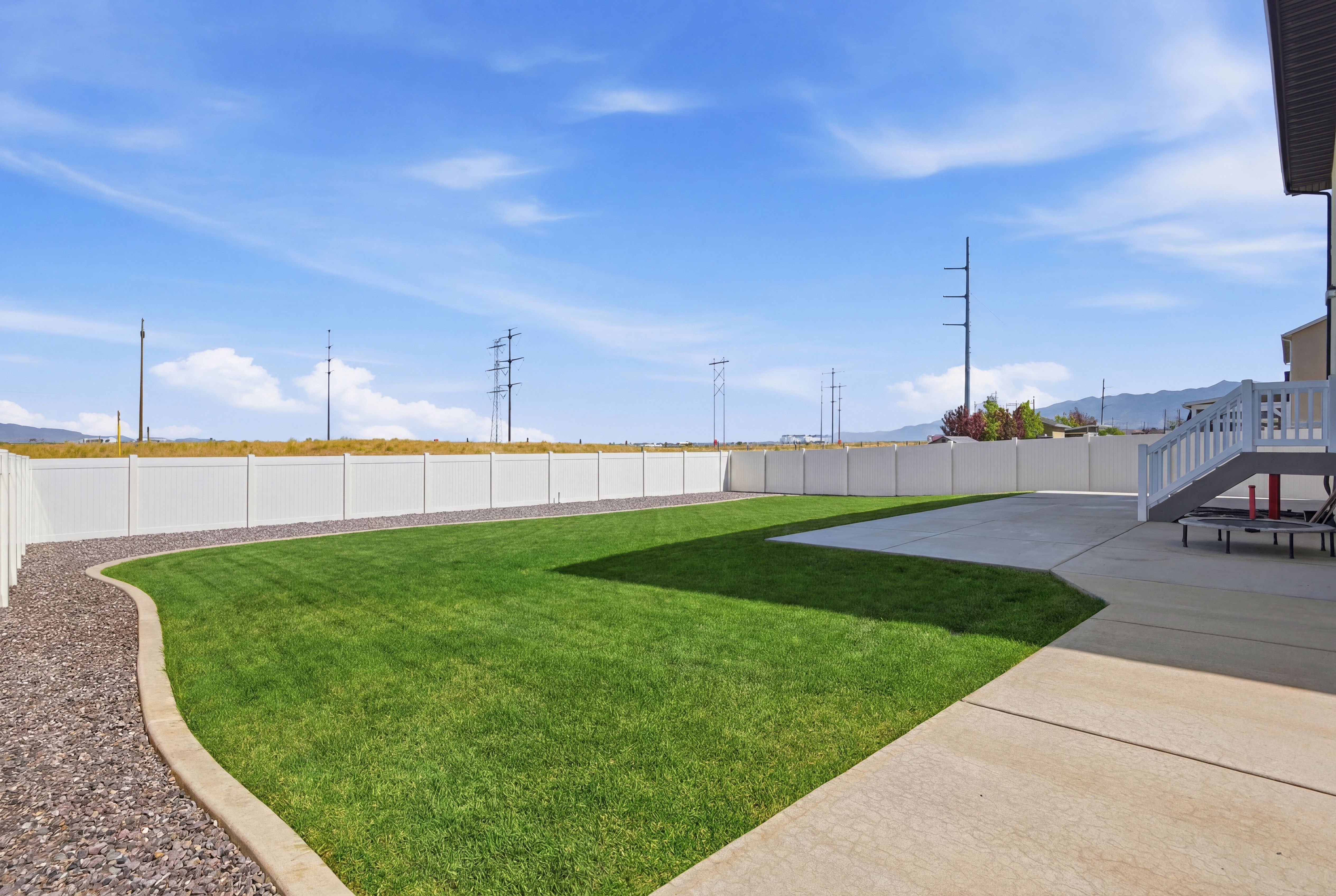 Expansive backyard featuring a green lawn, concrete patio, and a white privacy fence