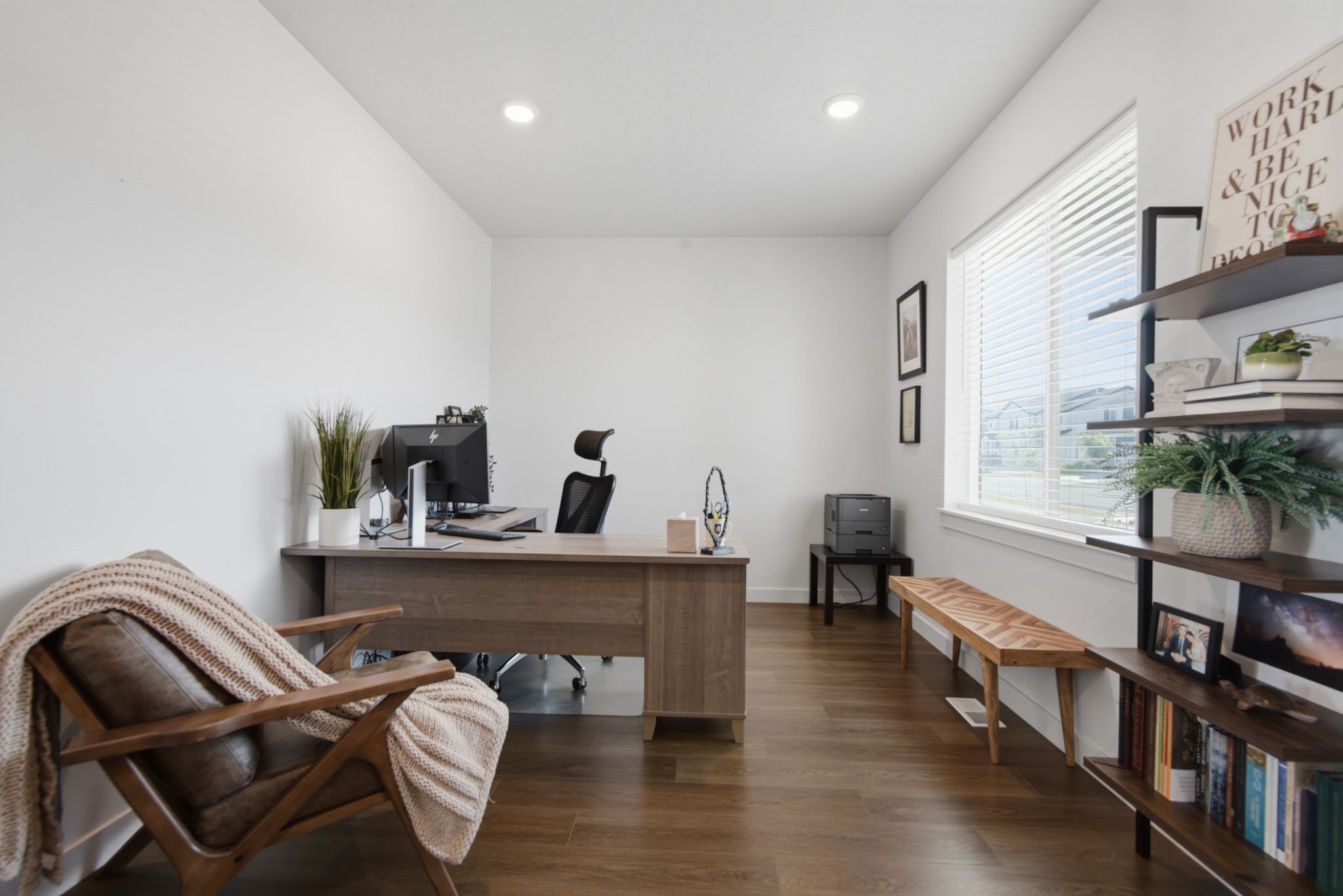 Bright room featuring a large window with white blinds, wood-finish flooring, recessed lighting, and built-in shelving
