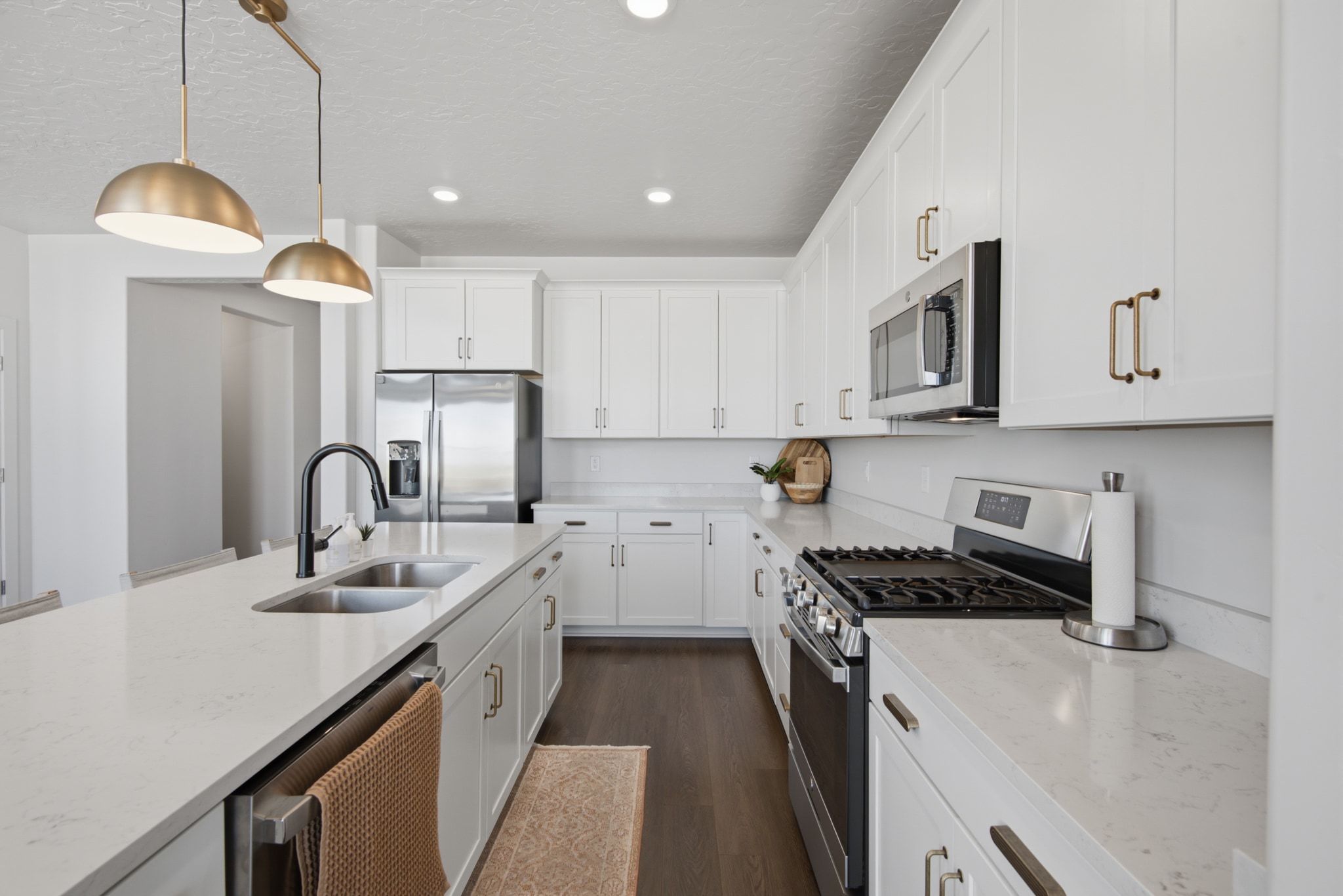 Modern kitchen featuring an expansive center island with a double basin sink, white cabinetry with contemporary hardware, stainless steel appliances, and dark wood-finish flooring