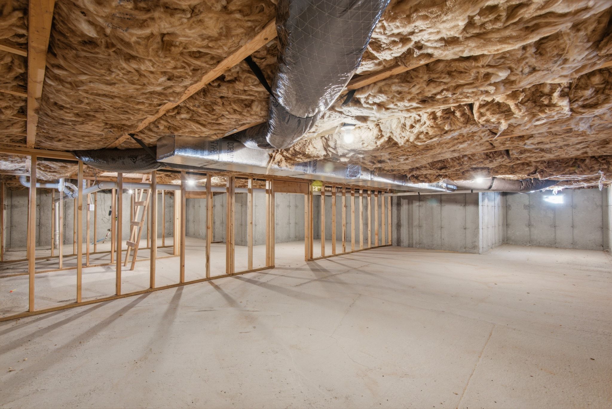 Expansive unfinished basement featuring concrete flooring, exposed wooden framing, and visible insulation