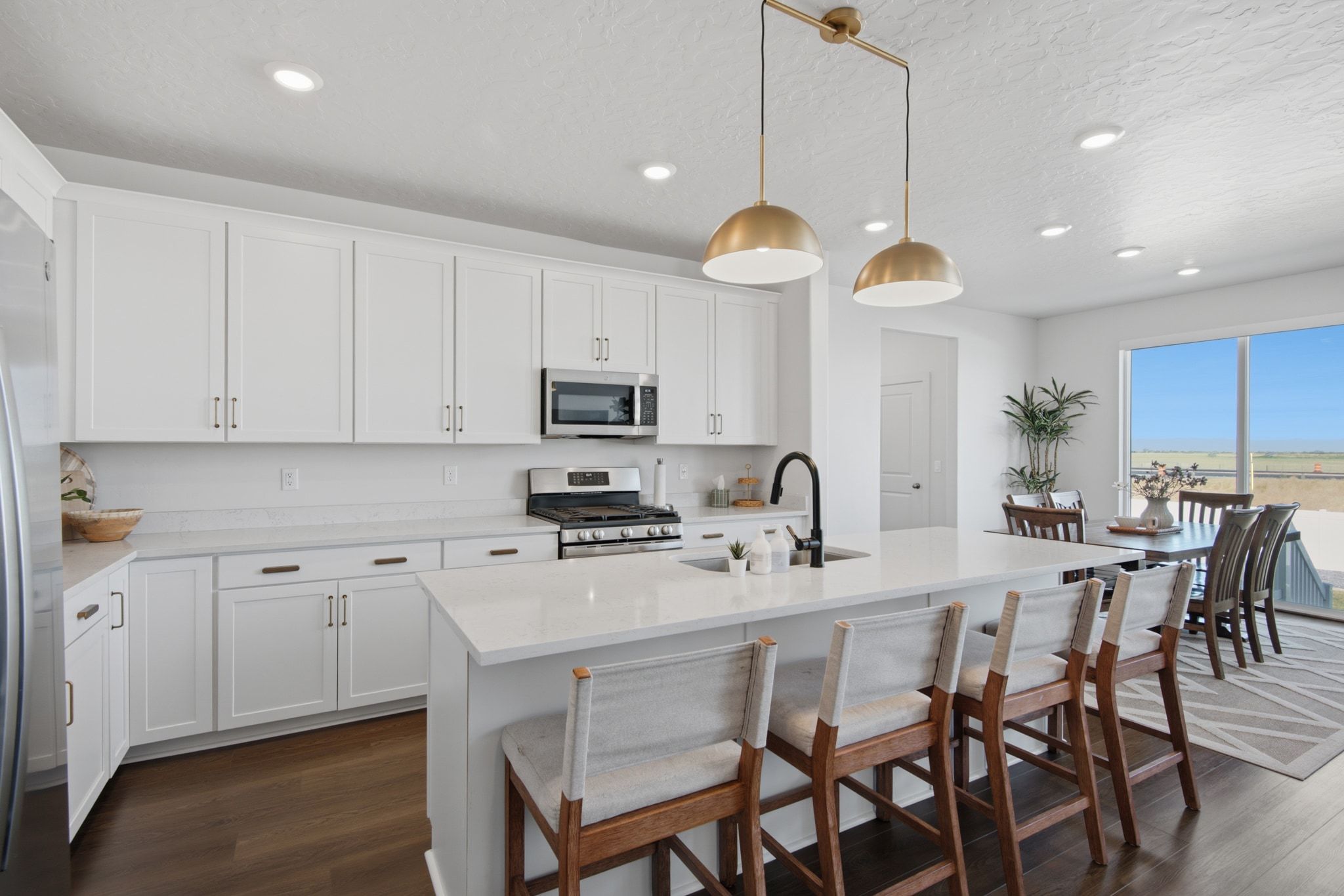 Modern kitchen featuring white cabinetry, stainless steel appliances, a white quartz island with seating, a matte black faucet, and wood-finish flooring