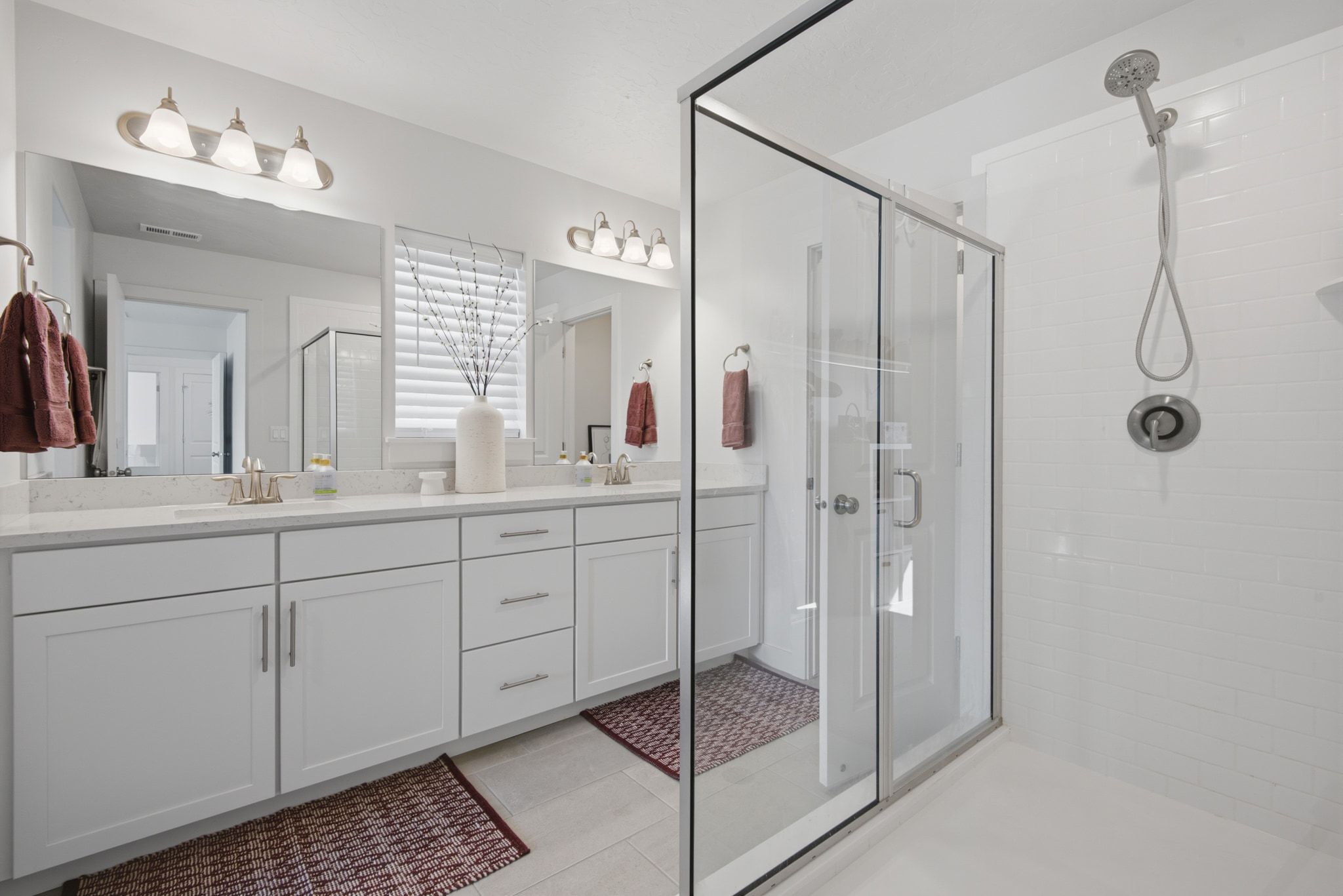Modern bathroom featuring a dual vanity with white shaker-style cabinetry, light-colored countertops, and two framed mirrors