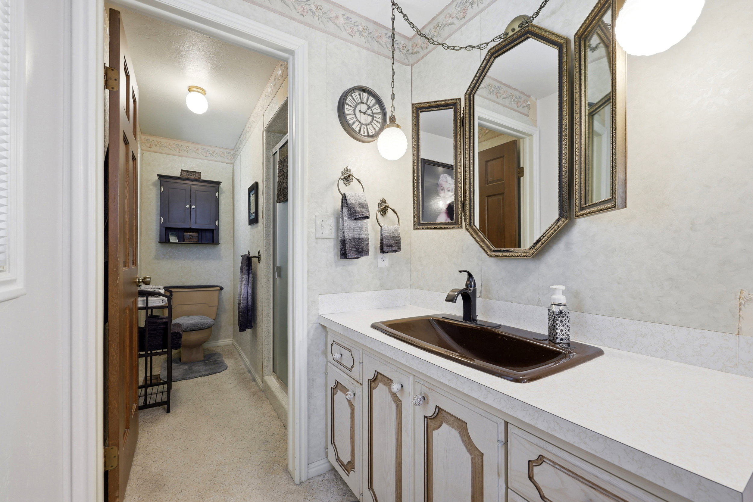 Bathroom featuring a vanity with a dark brown integrated sink, white countertop, and antique brass framed mirror