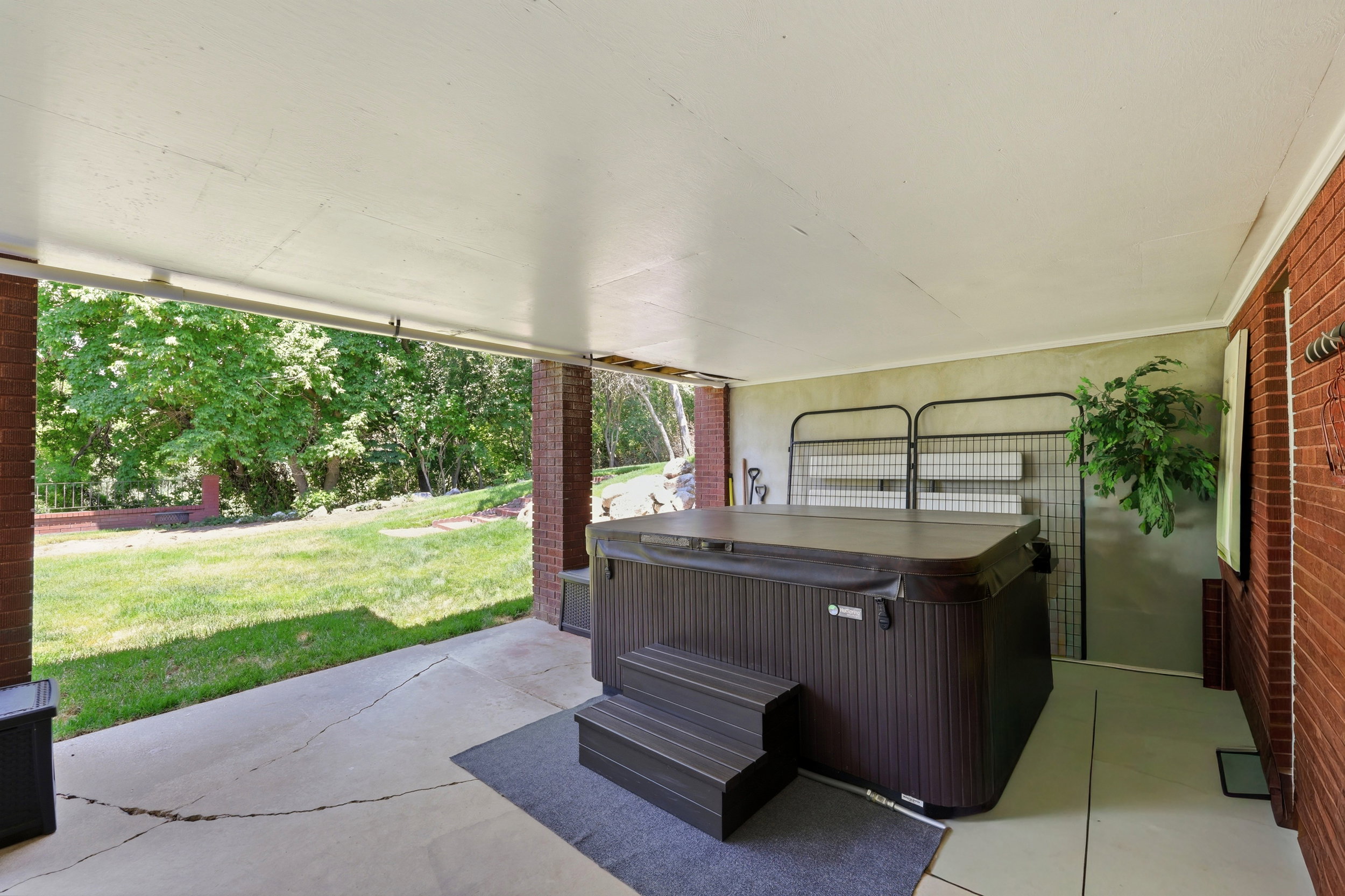 Covered patio with a dark-toned hot tub and steps