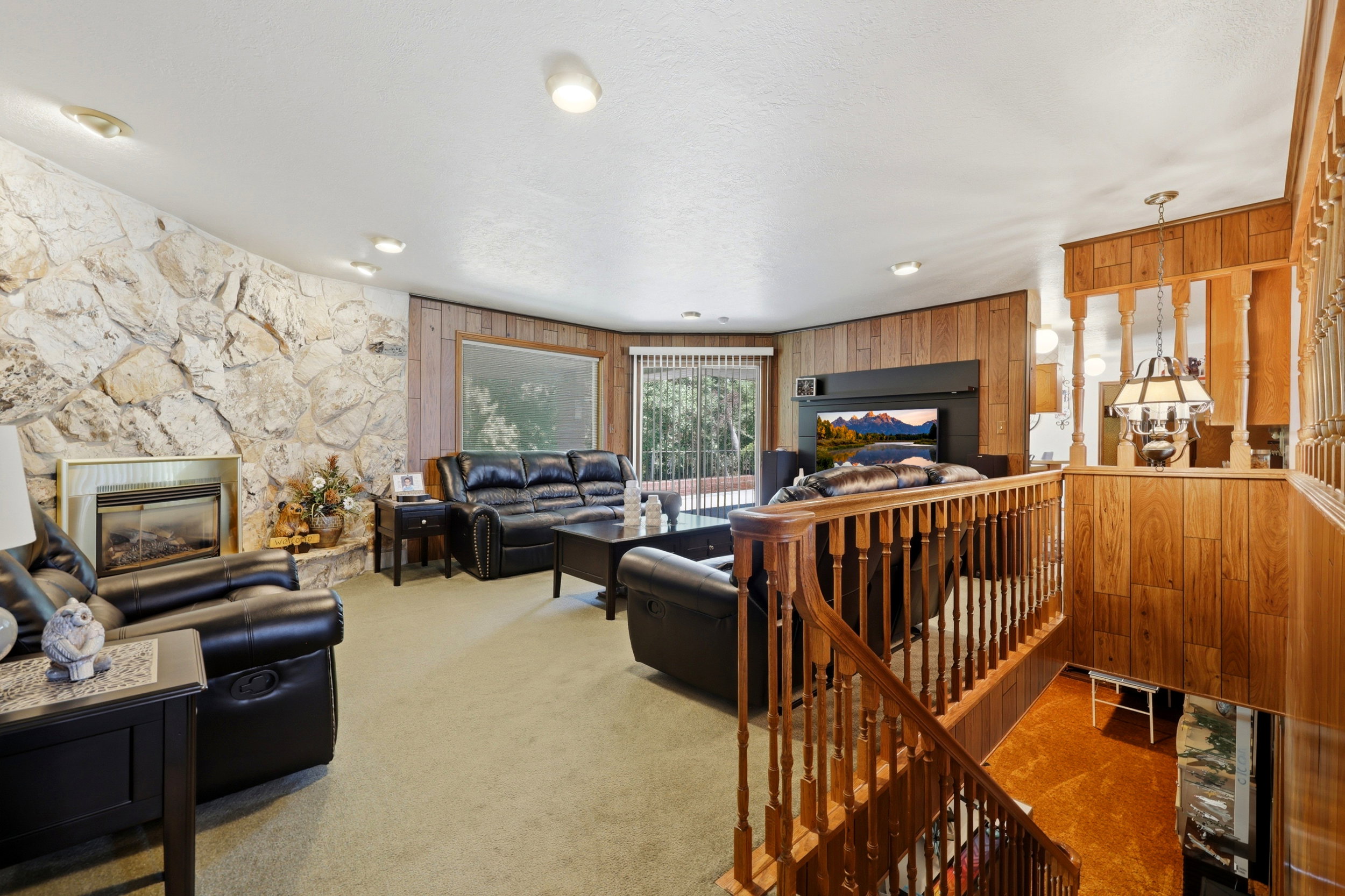 Living area featuring a stone accent wall with an inset fireplace, wood-paneled walls, and soft carpeting