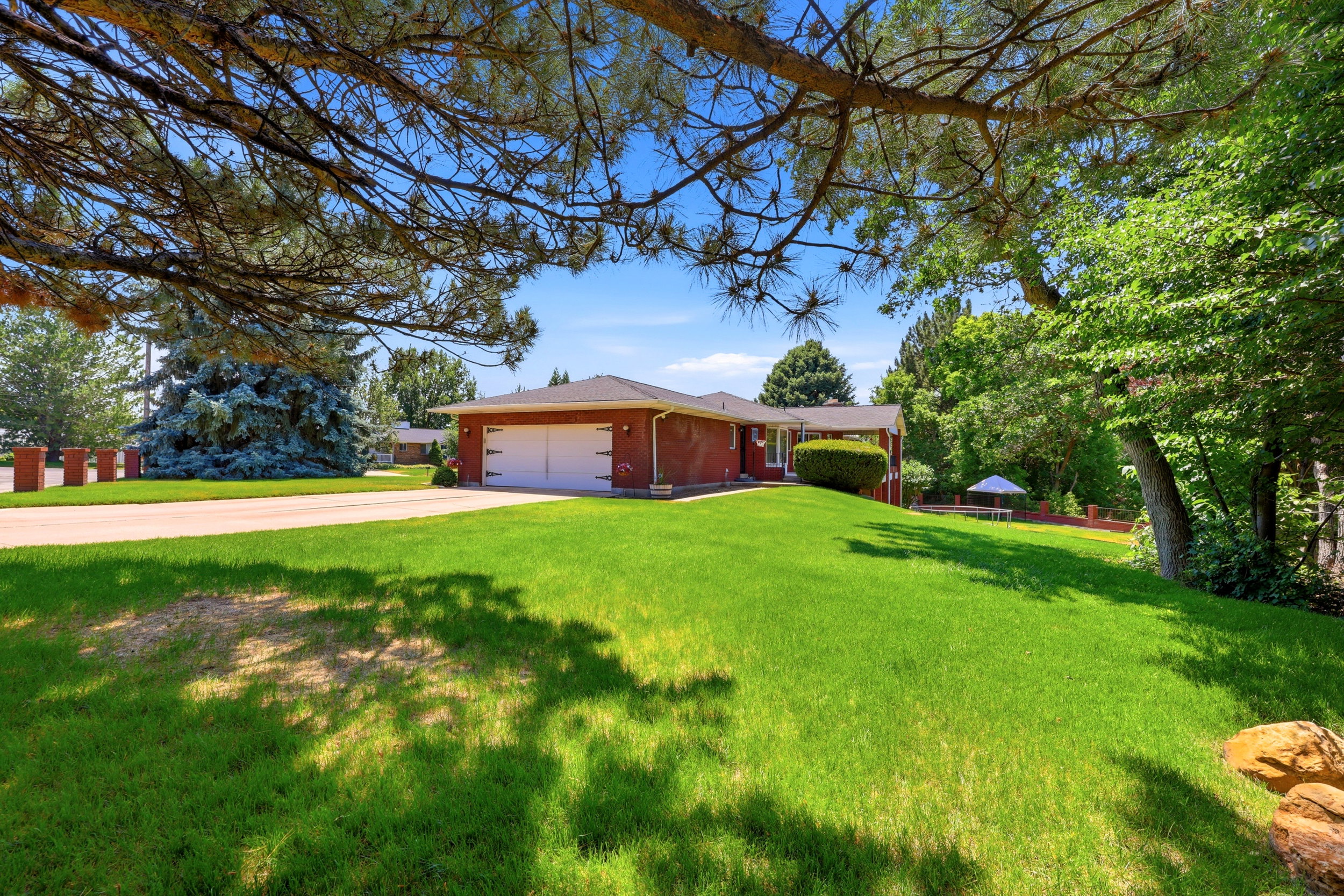 Expansive front yard featuring a manicured lawn, mature trees, and a brick exterior home with an attached garage