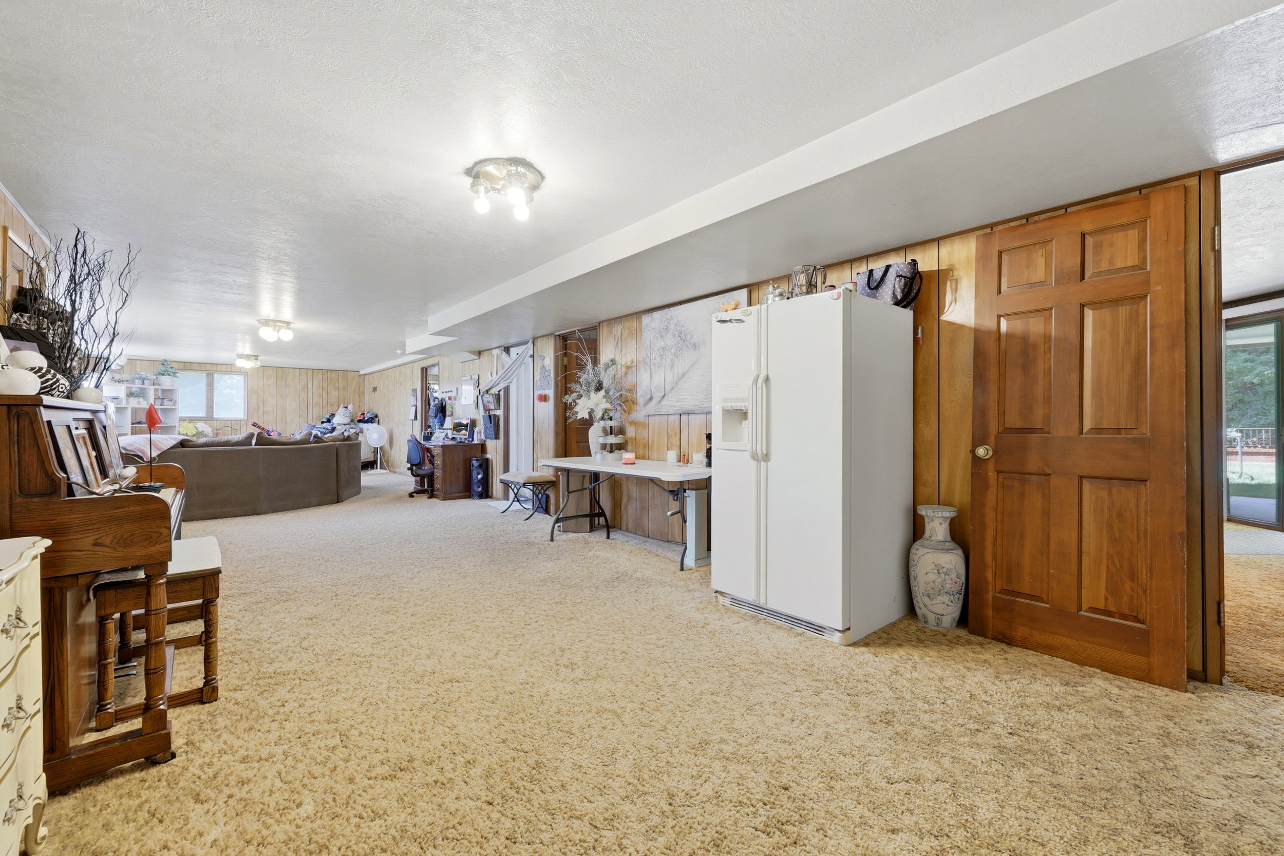 Spacious entertainment area with neutral-toned carpeting, wood paneling, and ceiling-mounted lighting