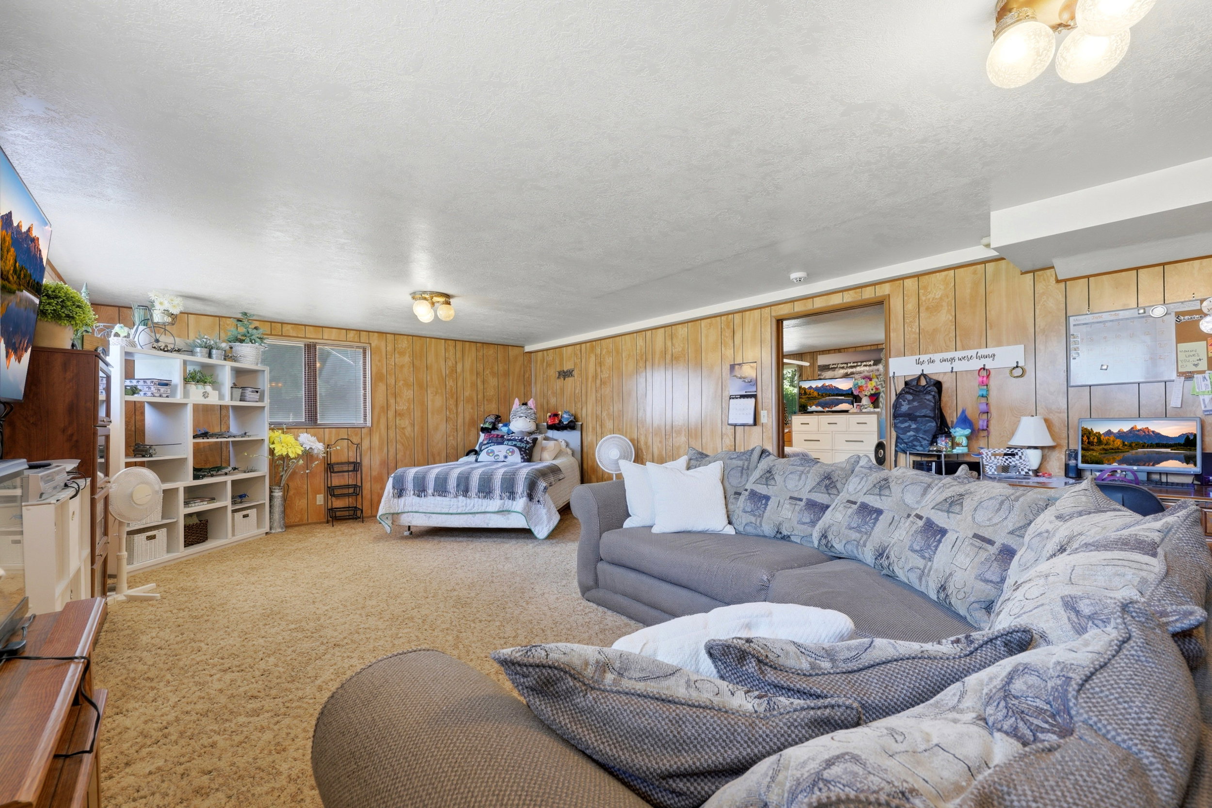 Spacious room featuring wood paneling, light-colored carpeting, two windows, and overhead lighting fixtures