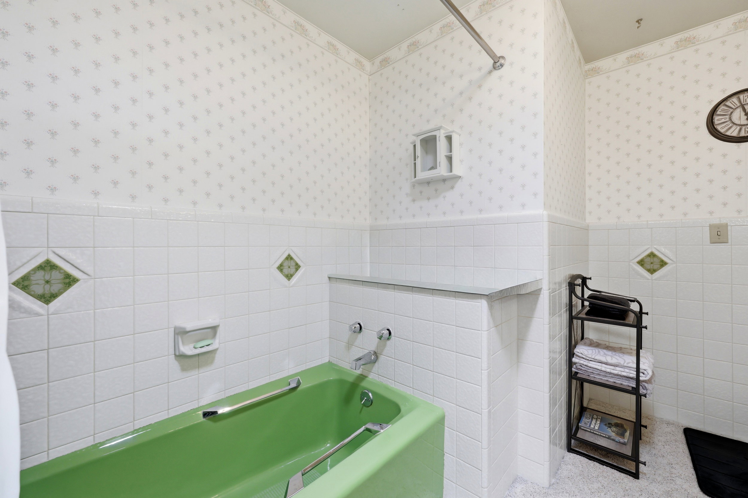 Bathroom featuring a vibrant green built-in tub, white subway tile surround, patterned wallpaper, and a chrome shower rod