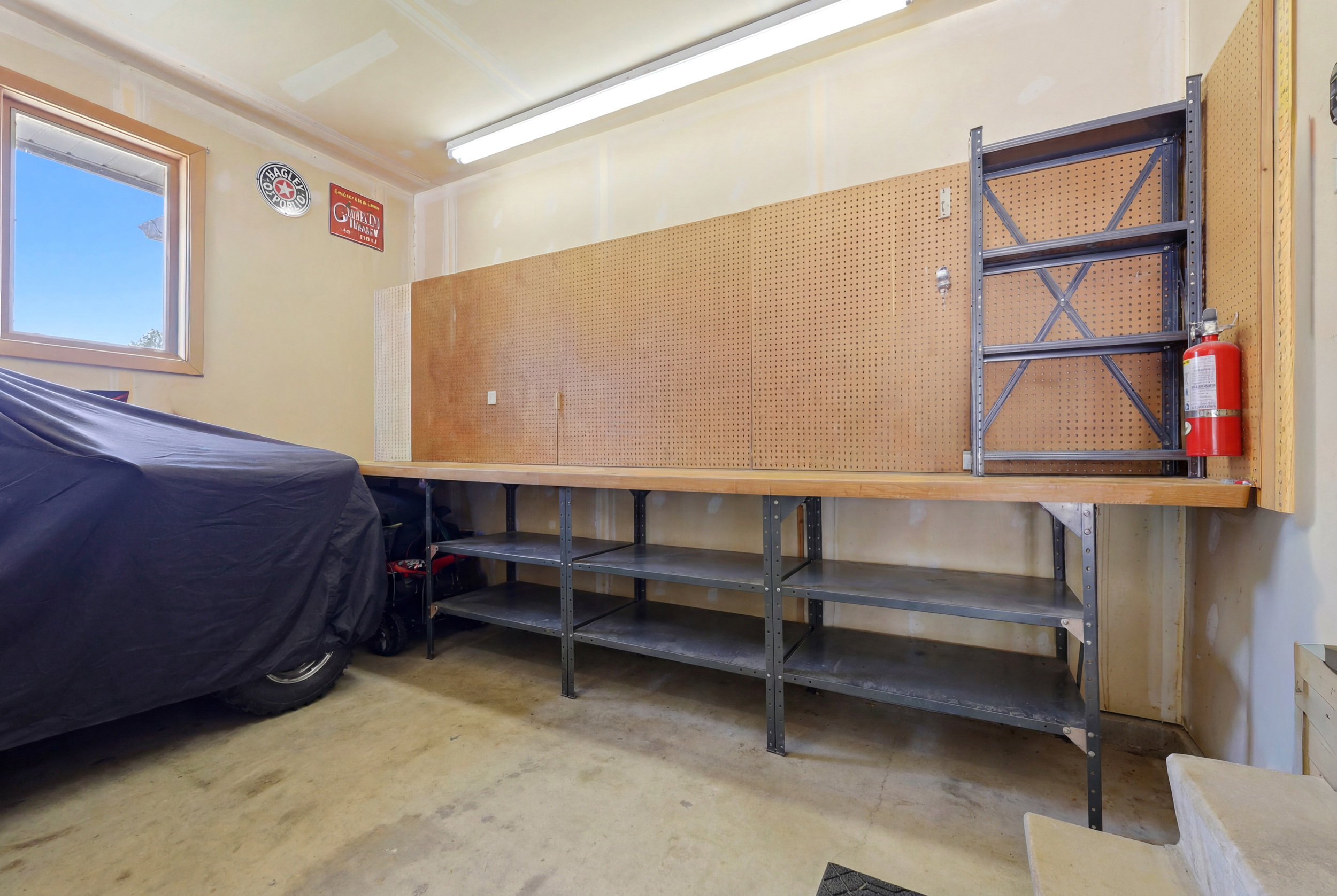 Garage workshop area featuring a built-in workbench with underlying shelving, extensive pegboard organization, and a prominent window providing natural light