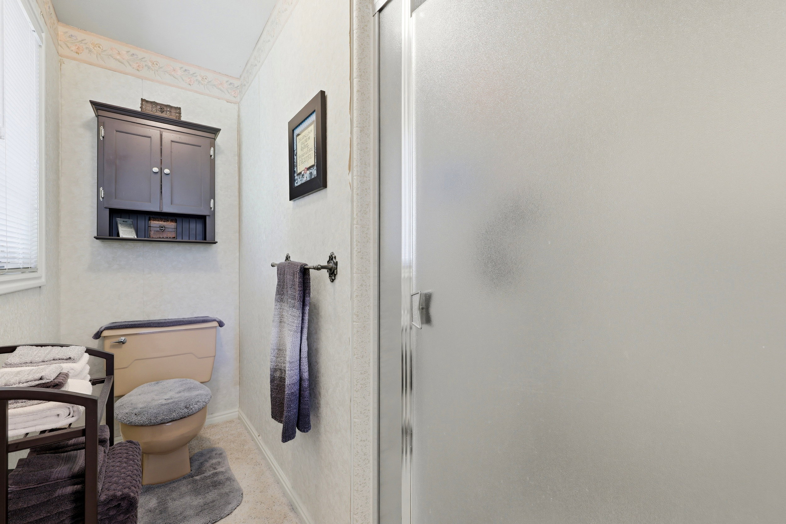 Bathroom featuring a frosted glass shower enclosure, wall-mounted storage cabinet, and window with blinds