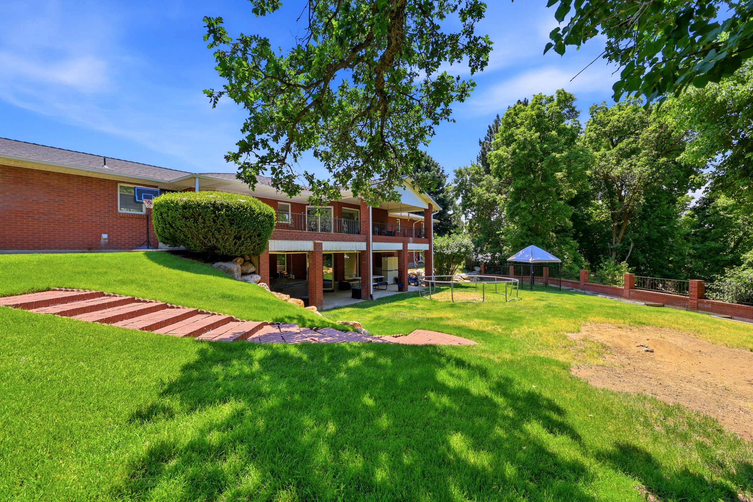 Spacious rear exterior featuring a red brick facade, tiered patios, an expansive lawn, and a covered gazebo