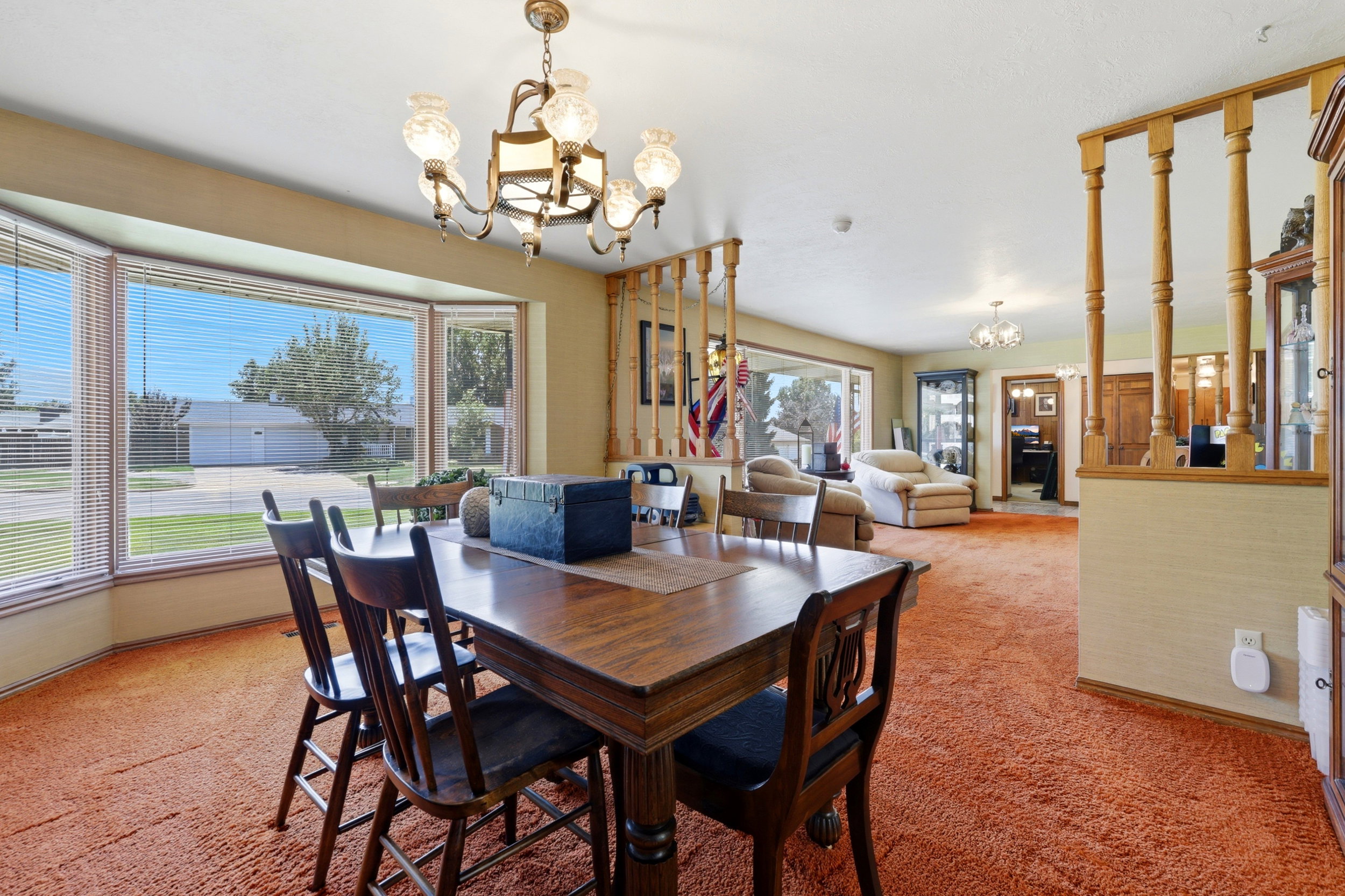Formal dining space featuring a large bay window with blinds, a multi-arm chandelier, and orange carpeting